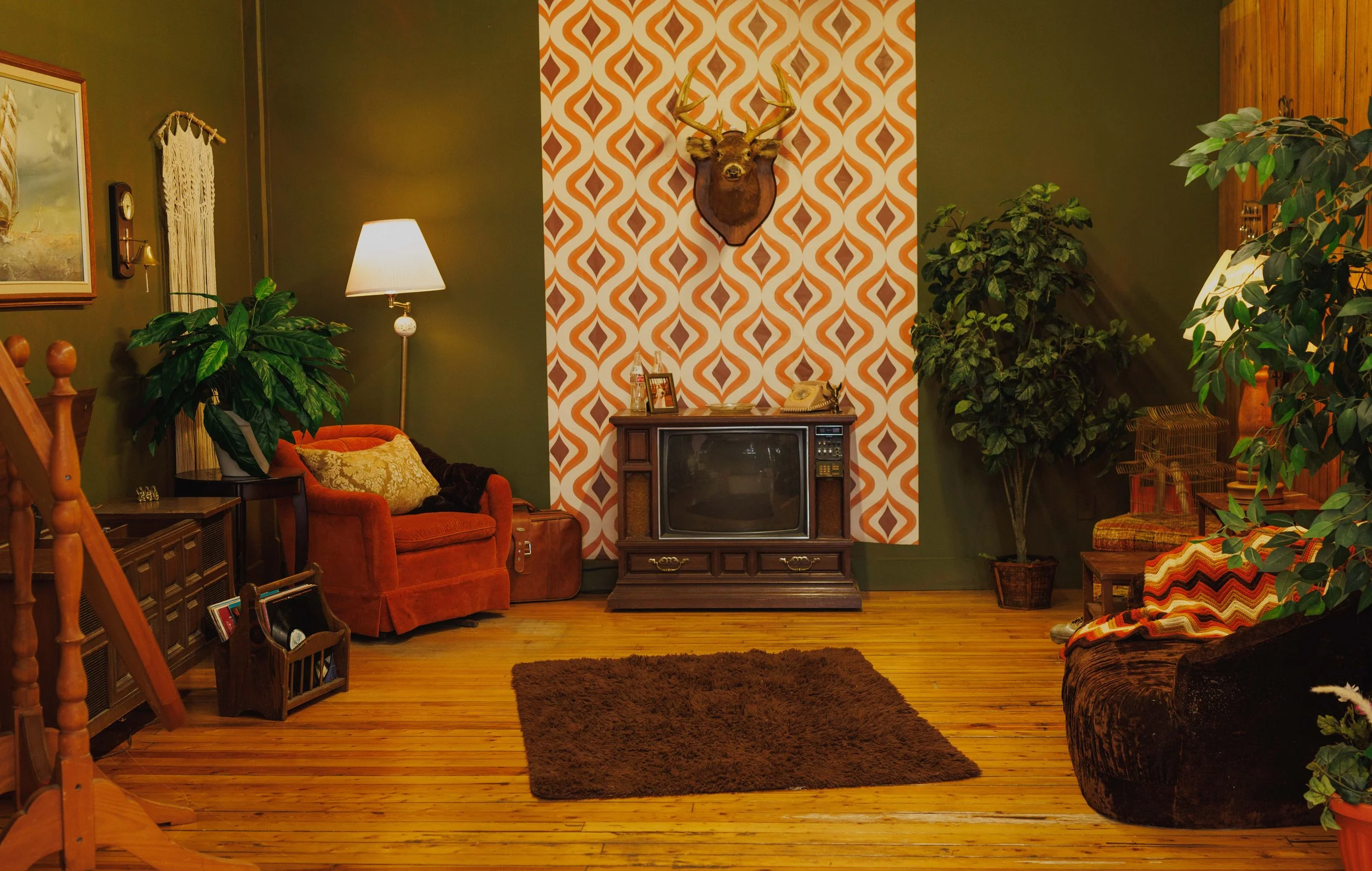 70s retro living room photography set featuring orange patterned wallpaper, vintage television, wood paneling, green walls, mid century furniture, shag rug, and nostalgic decor at Studio Ethereal