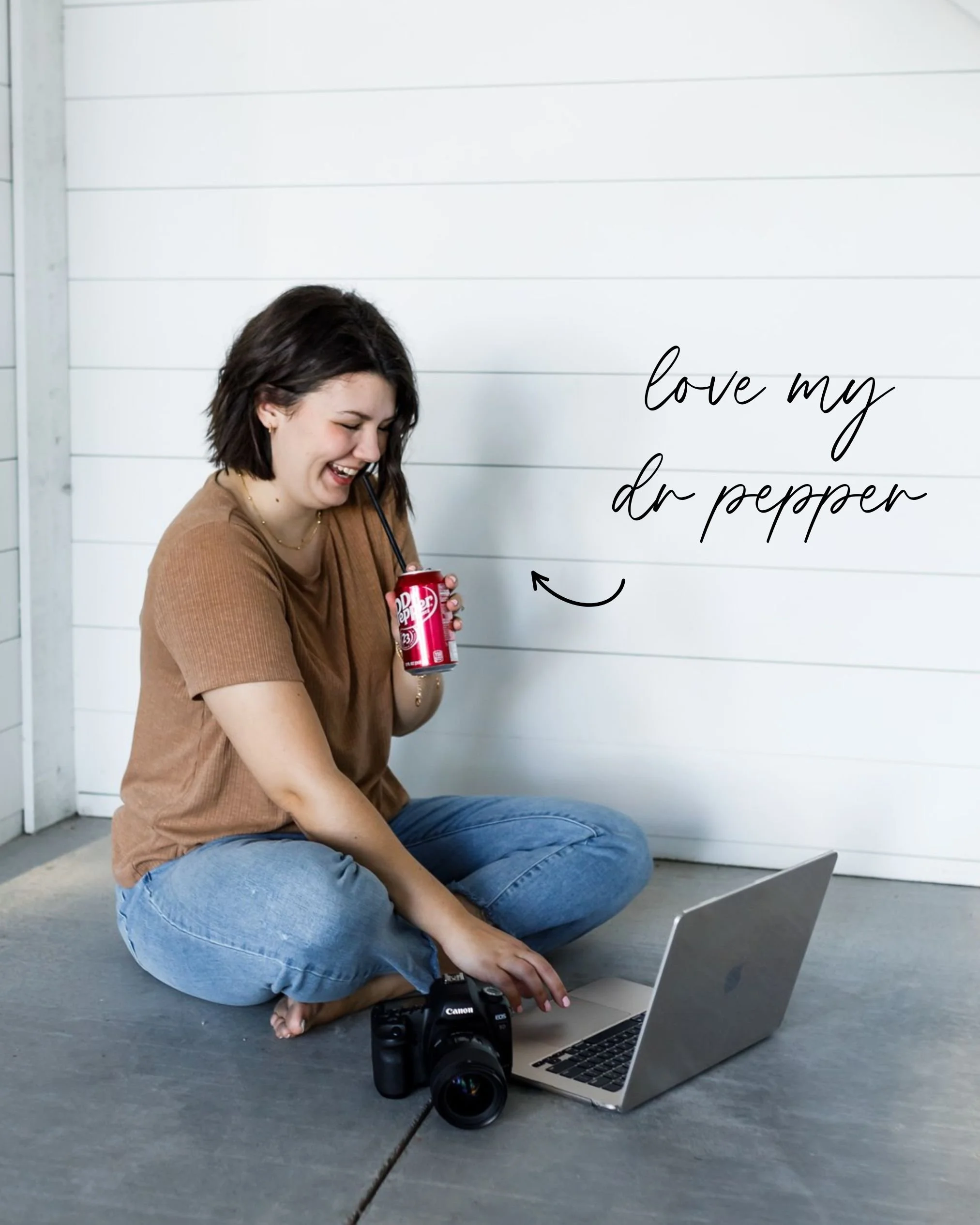 A woman sitting on the floor, smiling and drinking from a can, with a camera and a laptop in front of her. There is a handwritten note on the wall that says 'love my dr pepper'.