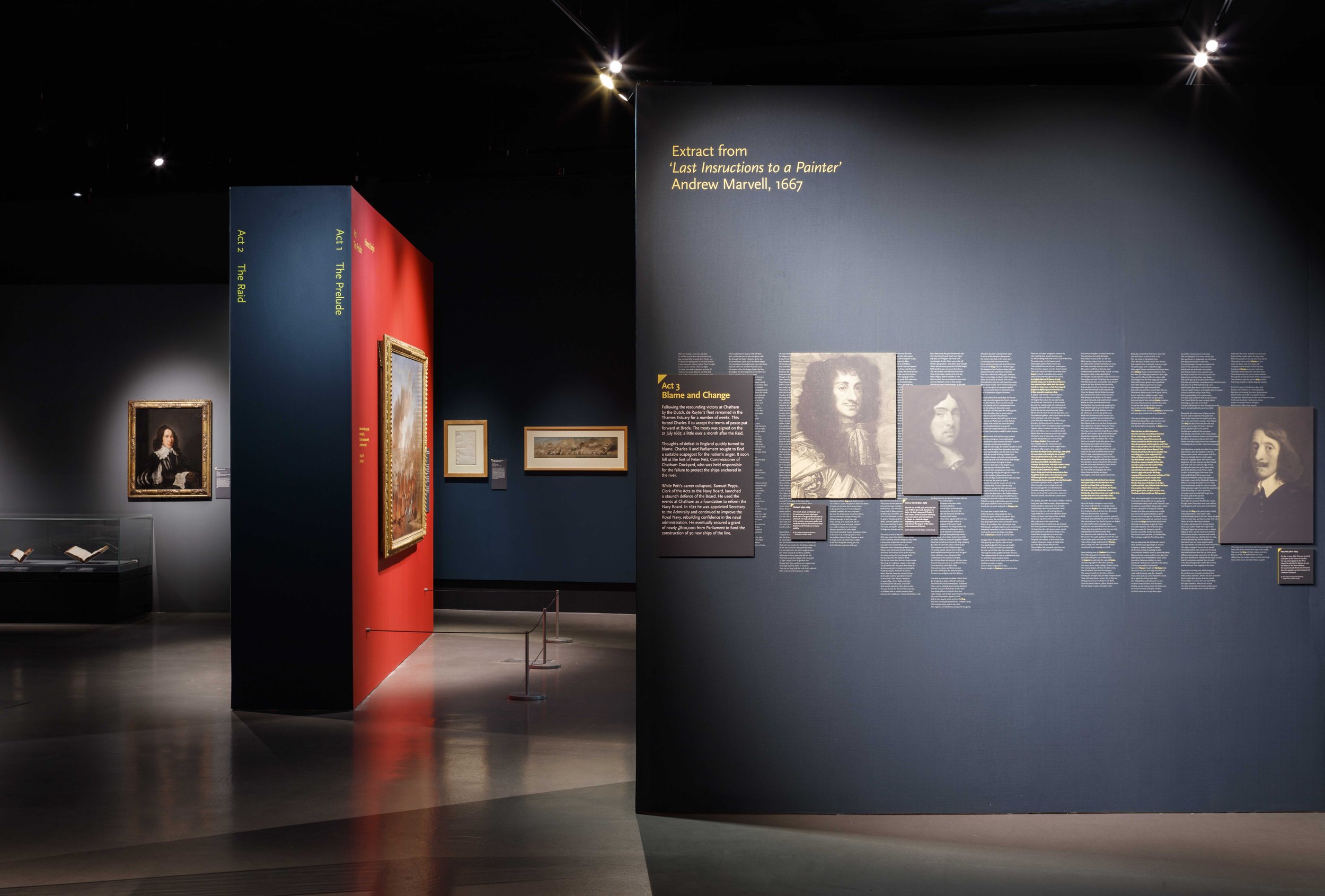 Gallery with framed paintings and showcases against blue and red walls. Exhibition themes are divided into Act 1: The Prelude, Act 2: The Raid, and Act 3: Blame and Change.