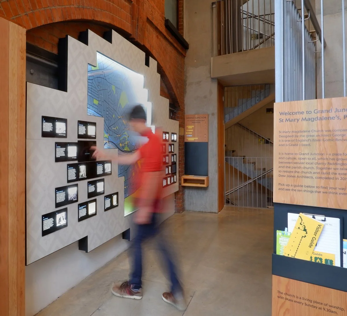 A person interacts with a touchscreen, next to a large local map and displays of backlit images and text.