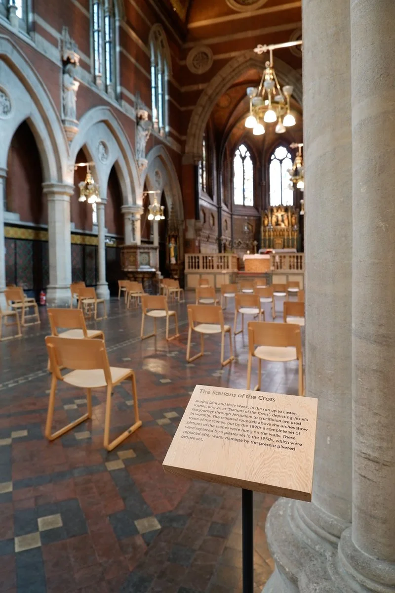 A small freestanding wooden sign provides information about the Stations of the Cross at the entrance to an ornate church space.