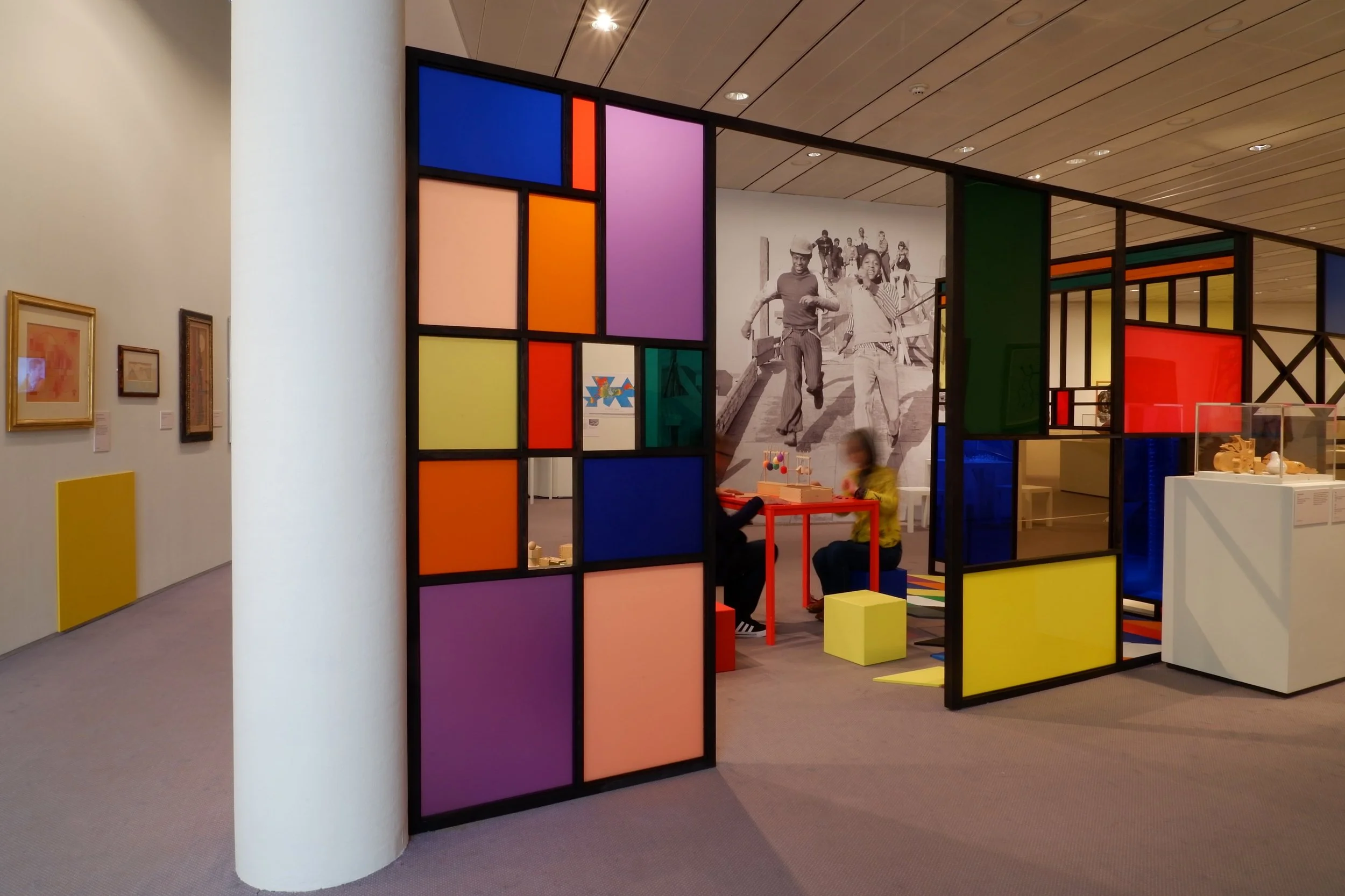 Colourful division walls by Eamon O'Kane in gallery displaying contemporary art. Interactivity for visitors and big photograph of children playing as graphic wallpaper.
