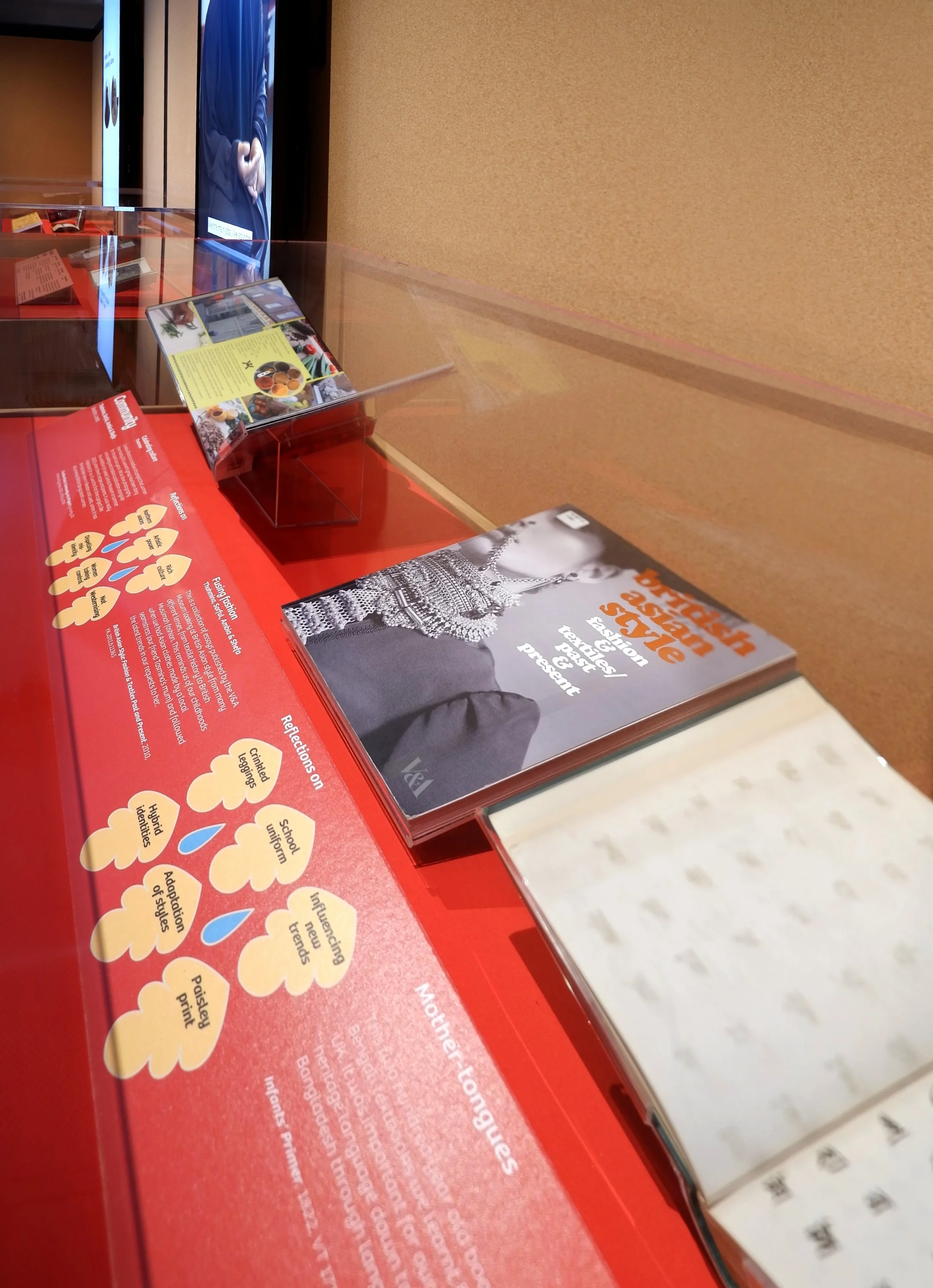 Showcase with books displayed open-mounted on clear acrylic mounts. The baseboard and the labels in front of the books are red. The labels contain information and pictograms.