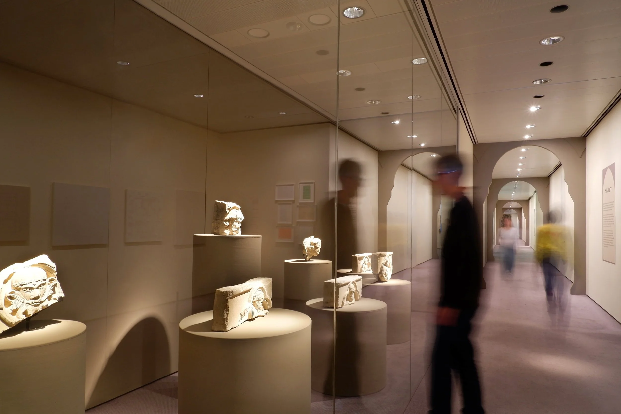Corridor with arched representing abstract interpretation of medieval cloisters in gallery space. Big glass vitrine with medieval fragments from cathedral displayed on cylindrical plinths of different height.