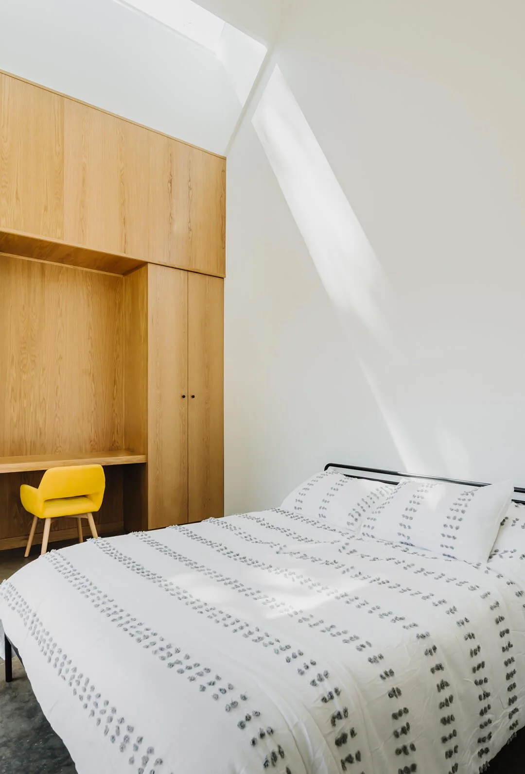 Bedroom with floor to ceiling white oak built-ins and a tall vaulted ceiling with skylight.