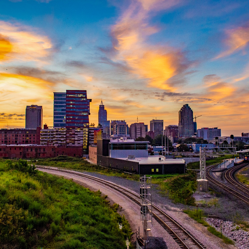 Sunset skyline of Raleigh-Durham, North Carolina with downtown buildings and railway tracks in the foreground.