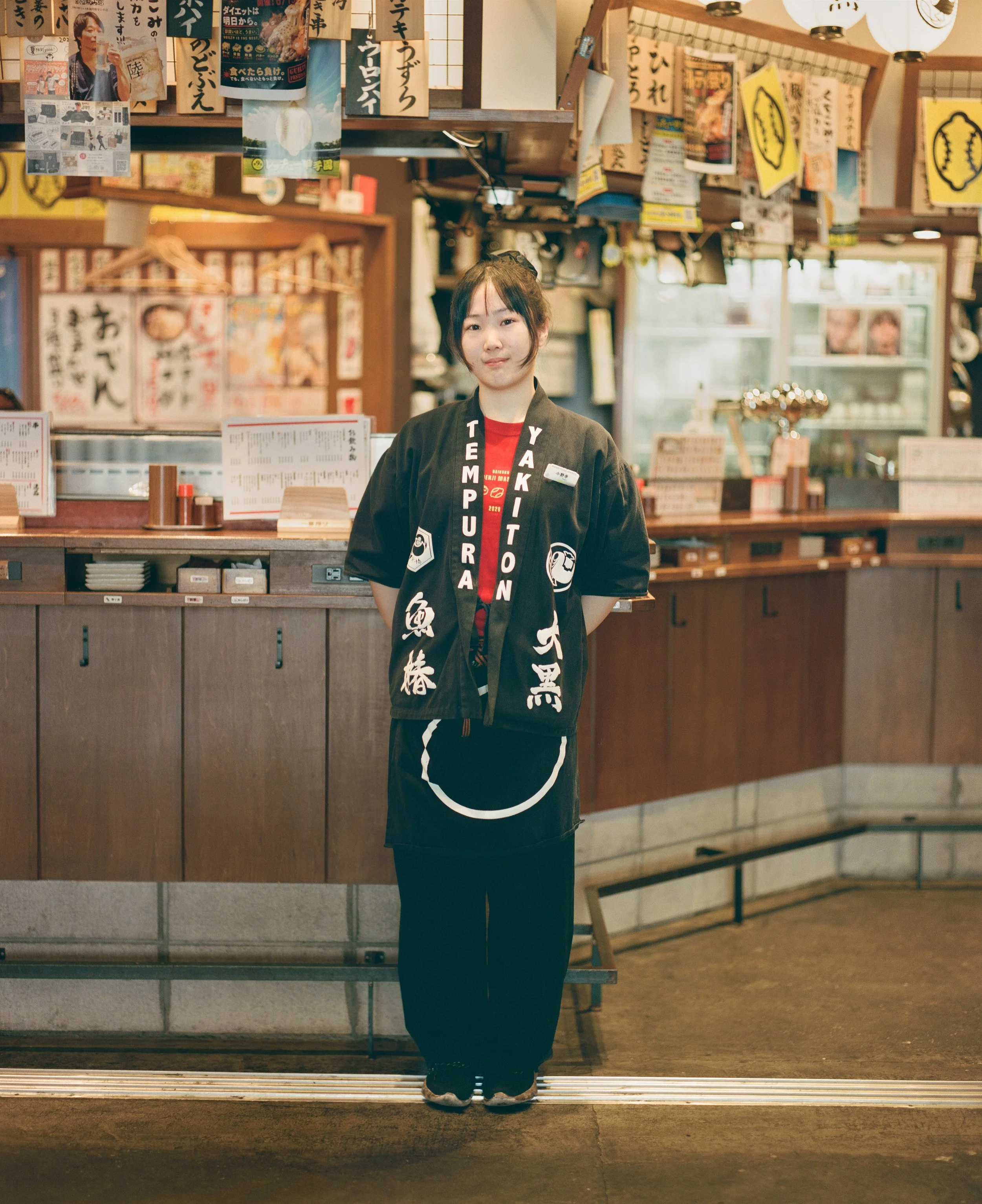Young woman working at an izakaya at Koenji station. The izakaya had few customers and she was able to spare a couple of minutes to let me photograph her. She stood reserved but confident - hands clasped behind her back, feet together and gaze steady