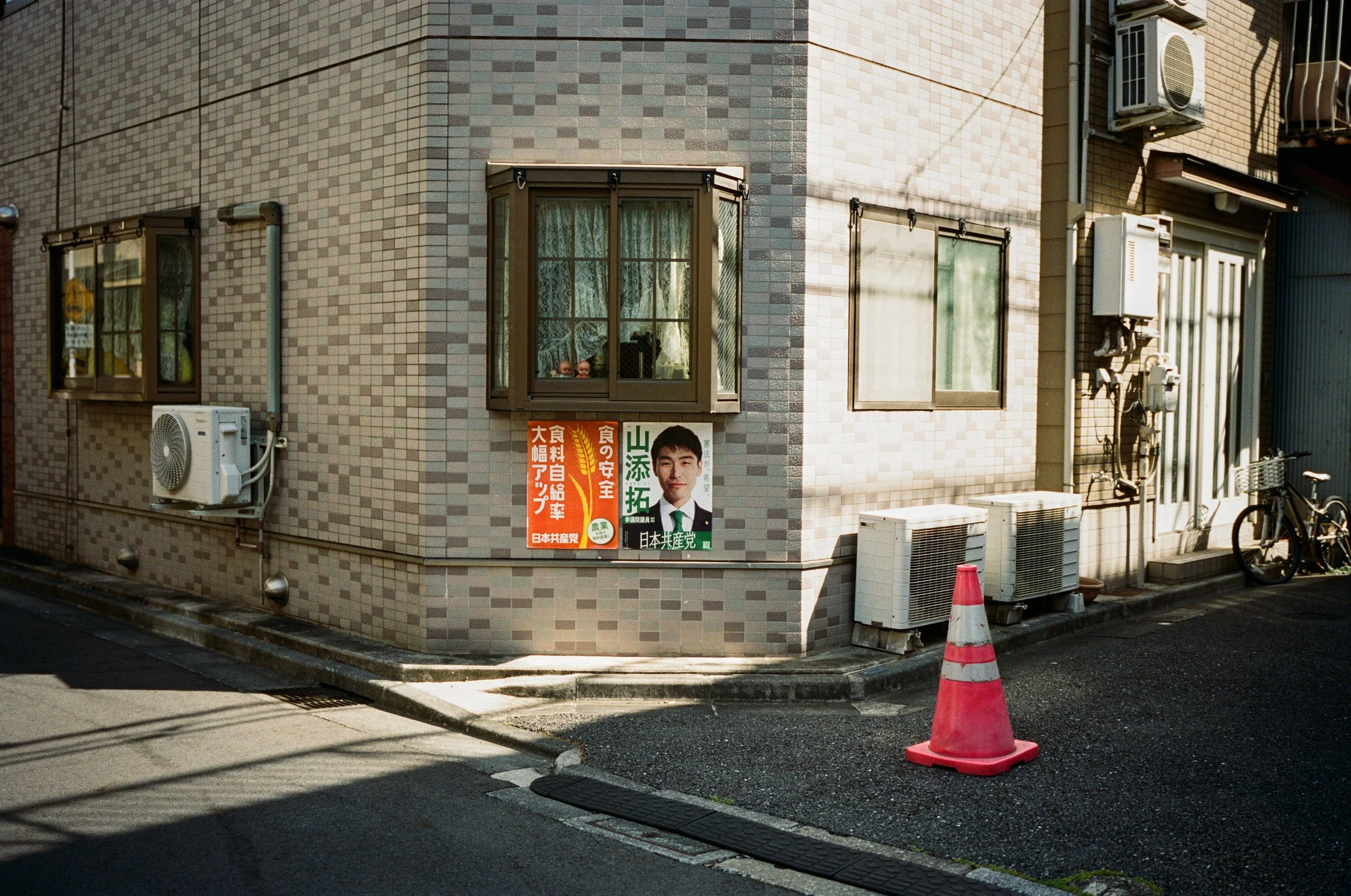 Japan Communist Party campaign posters in a narrow street near New-jinja. Two little dolls peek out from the window above.