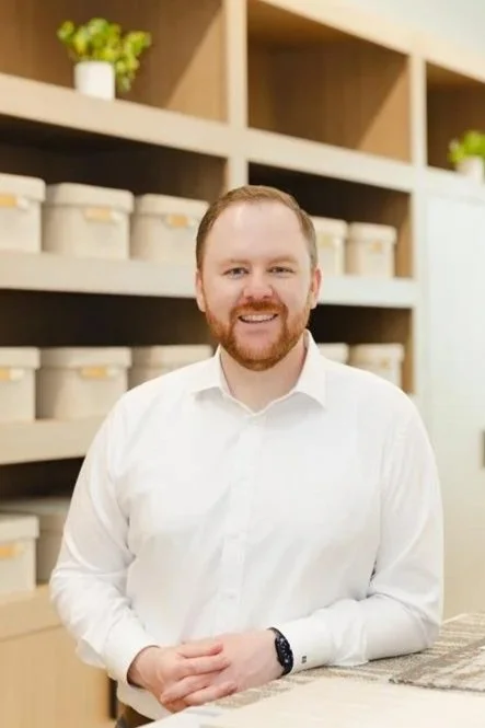 Smiling man in casual shirt standing in front of a wall with architectural diagrams.