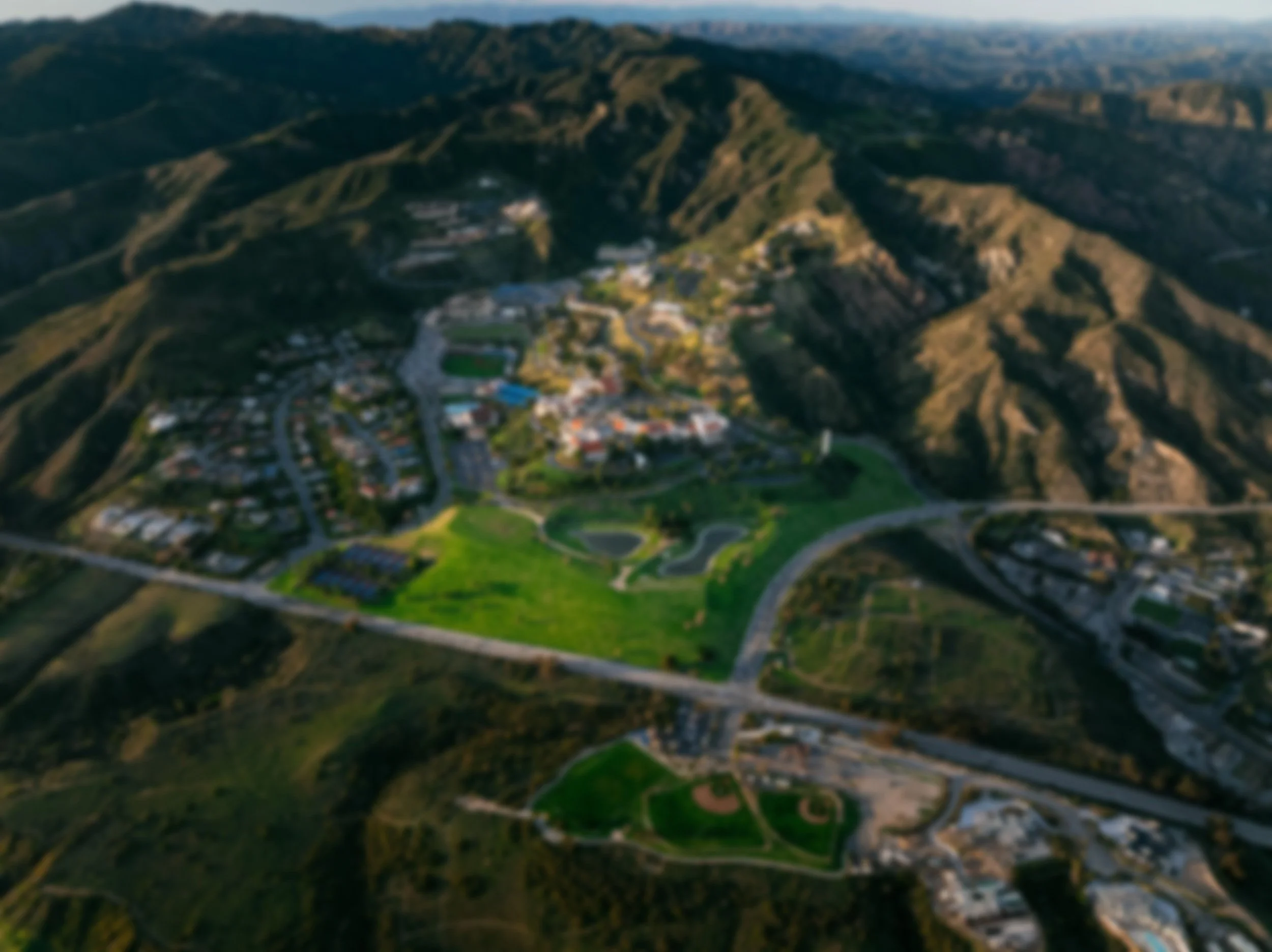 Aerial view of a residential neighborhood and park at the base of green hills.
