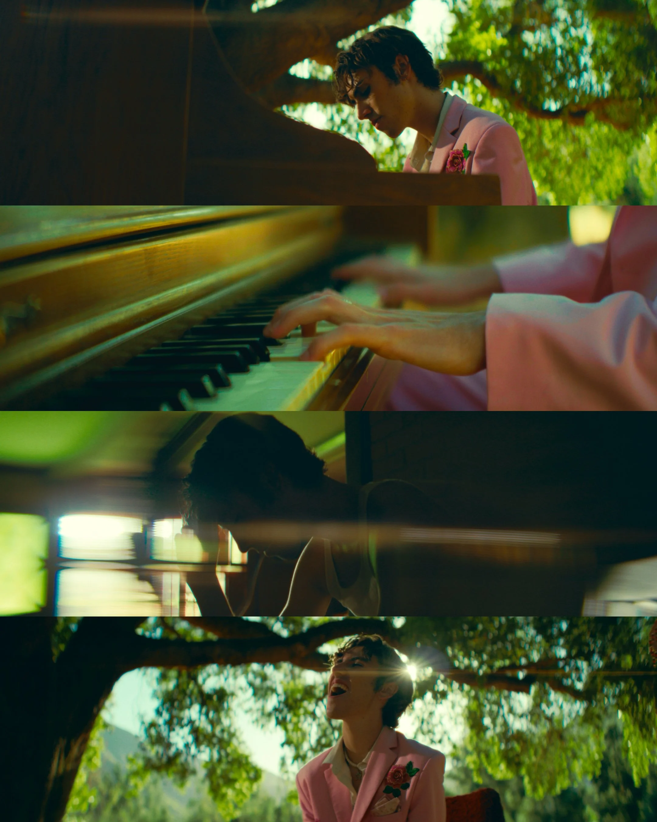 A young man with curly hair in a pink jacket playing the piano outdoors under a tree, singing and enjoying nature.