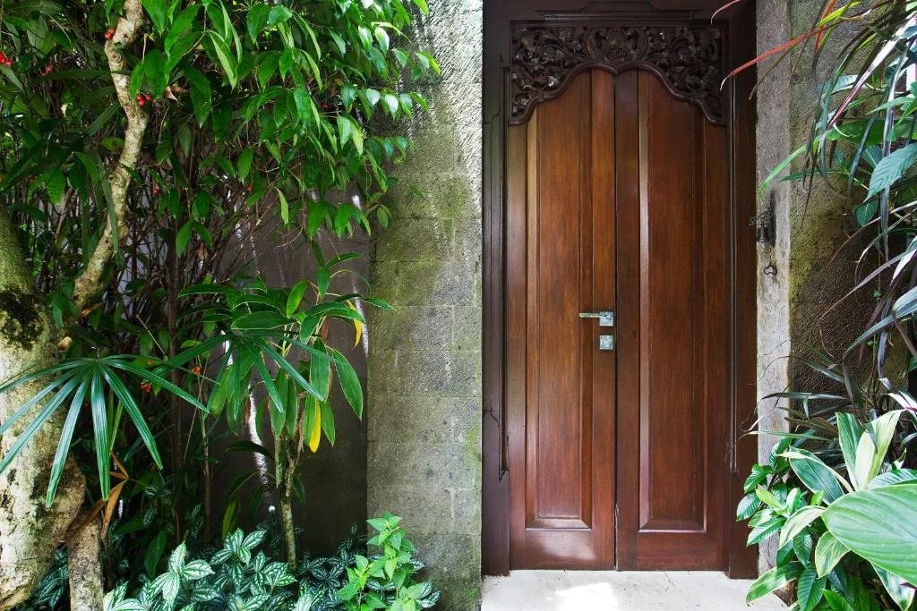 Wooden gate surrounded by lush green plants and trees in a garden setting.