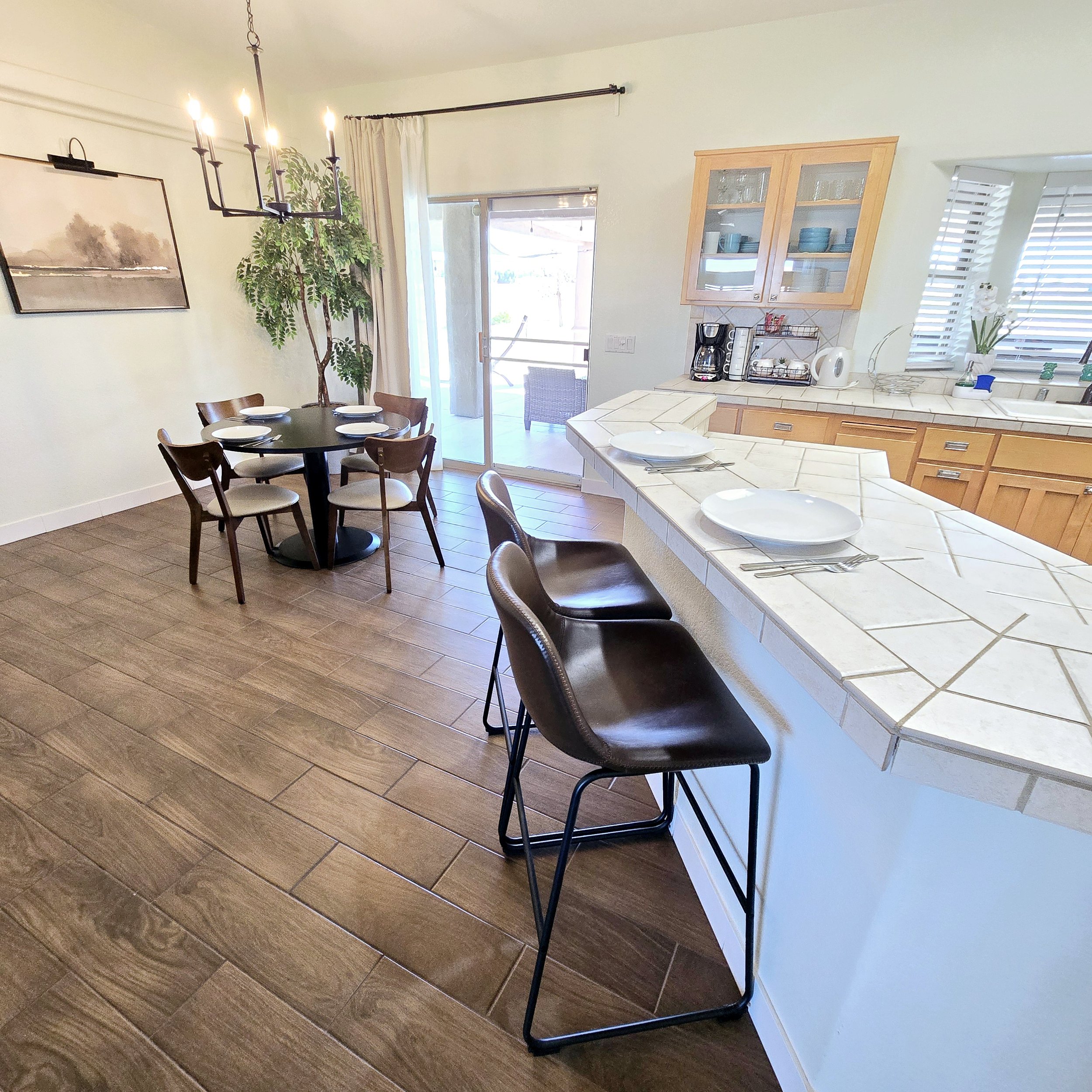 Kitchen and dining area with wooden floors, a round dining table with six chairs, a breakfast bar with three chairs, a sliding glass door leading to an outdoor patio, and kitchen cabinets with appliances.