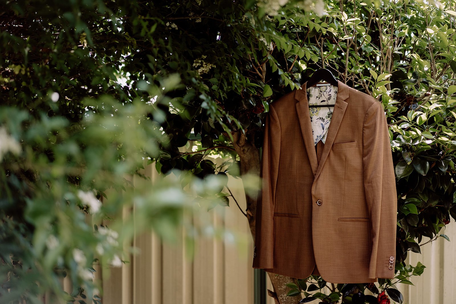 Grooms earthy brown suit jacket hanging in green tree