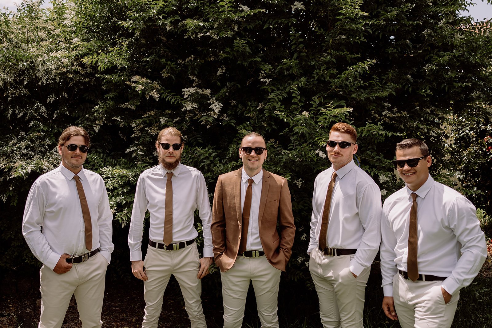 Groom and groomsmen standing together wearing cream pants and earthy brown tie