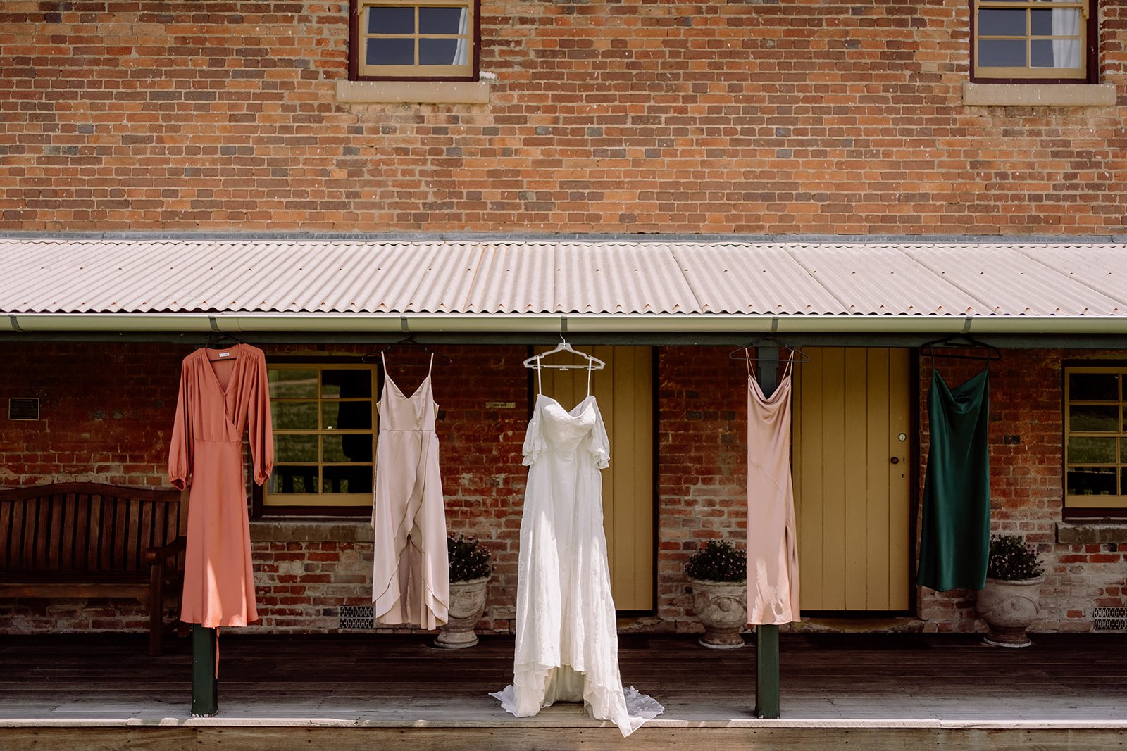 Bridal gown and mismatched bridesmaid dresses, hanging in front of Tocal Homestead