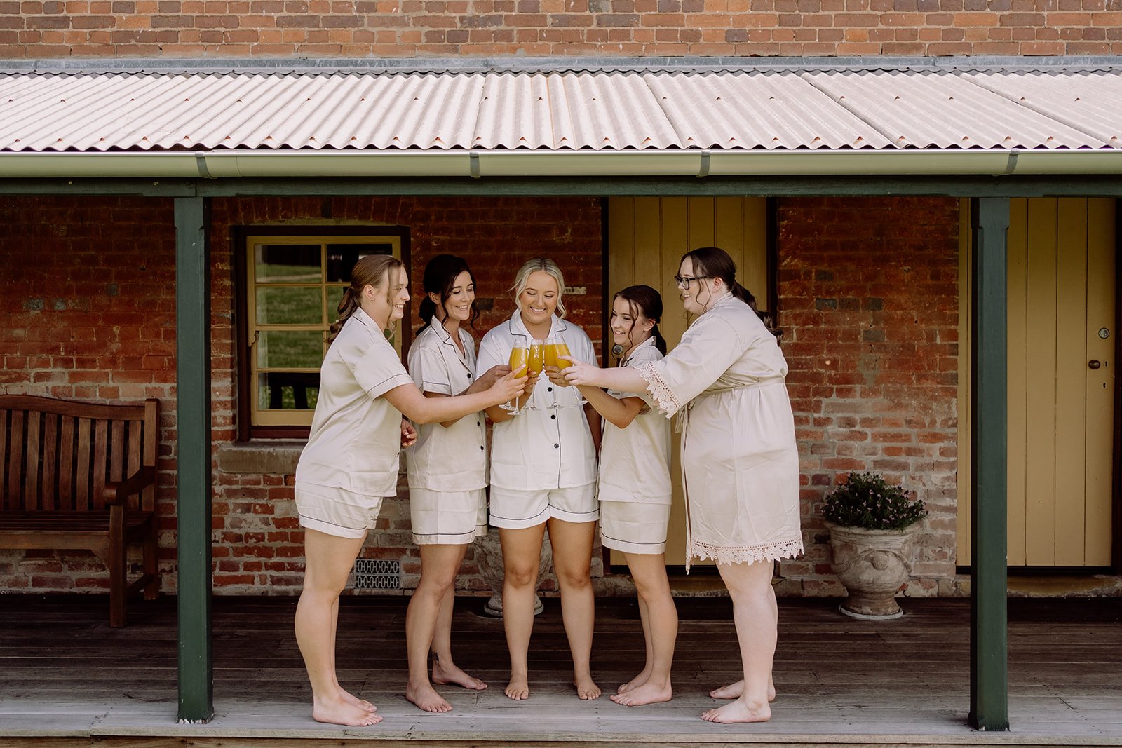 Bride and bridesmaids cheering and drinking together in front of Tocal Homestead