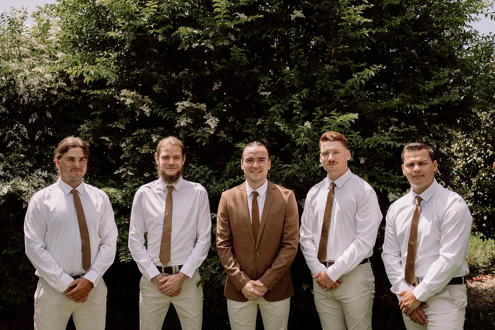 Groom and groomsmen standing together wearing cream pants and earthy brown tie