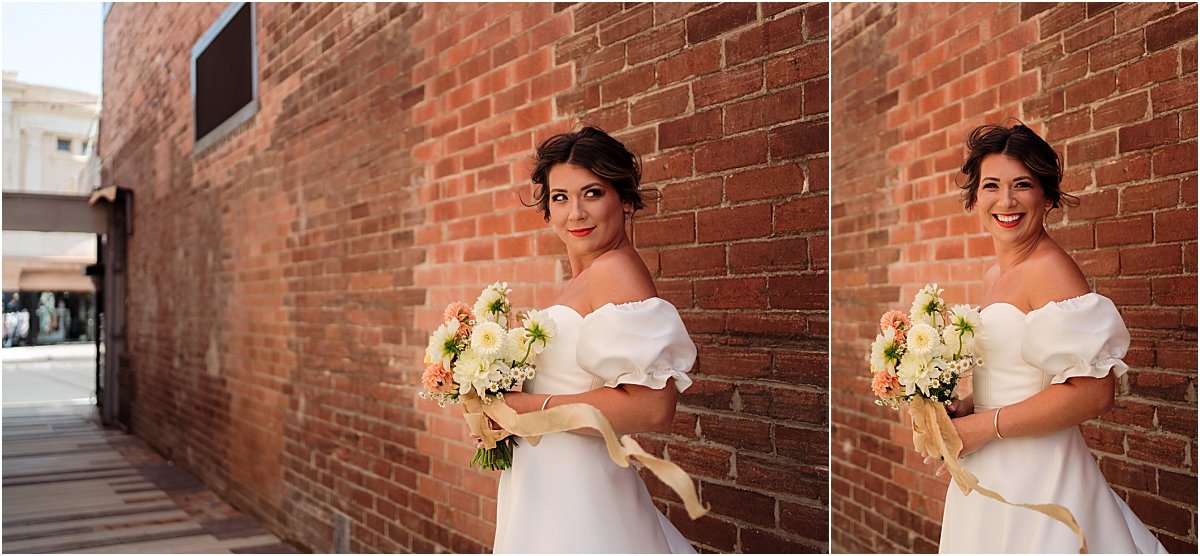 Bride standing in front of brick wall holding orange and yellow wedding bouquet