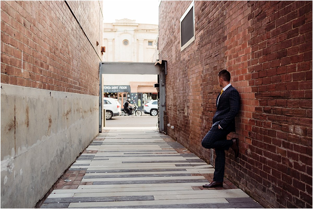 Groom standing in alleyway at the Owens Collective, wearing blue checkered suit and gold tie