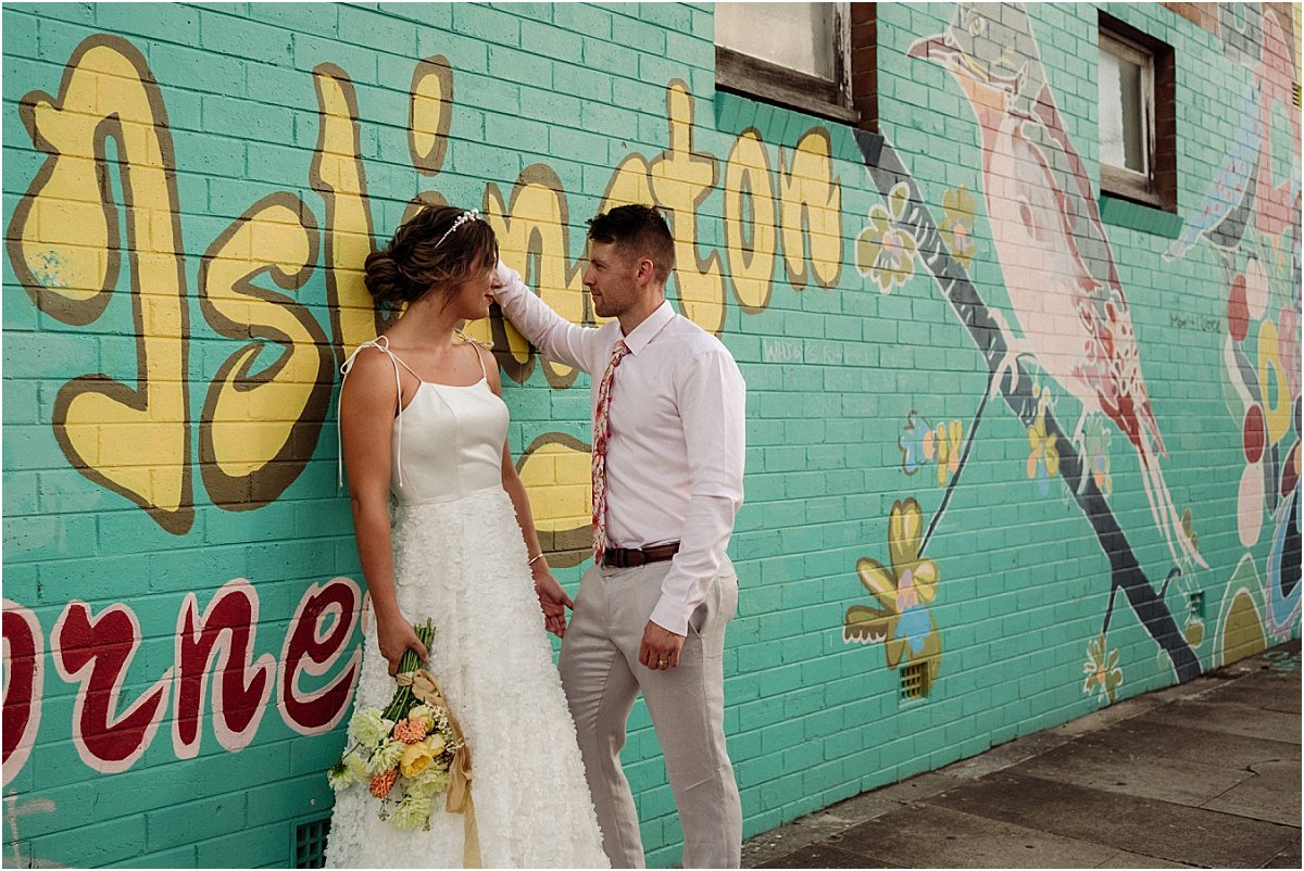 Bride and groom standing in front of bright green mural in Islington NSW