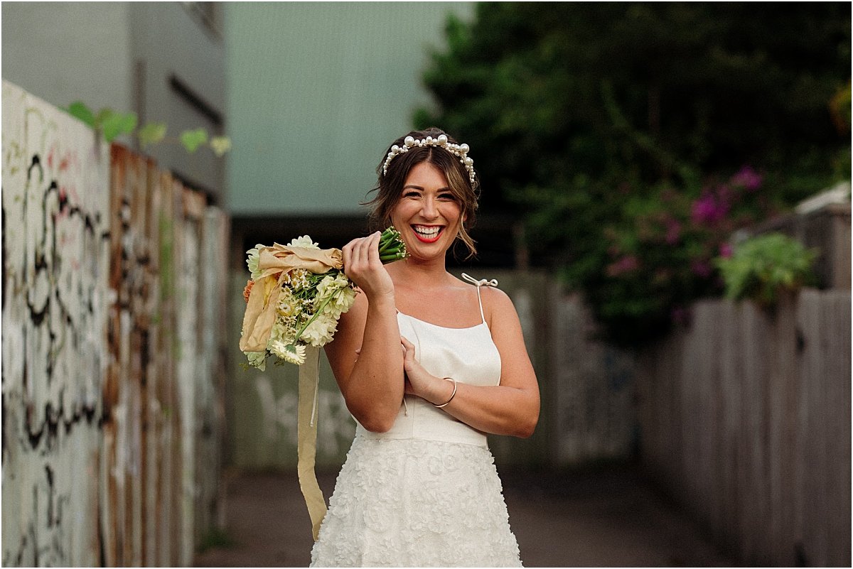 Bride standing in grafitti alleyway in Islington Newcastle NSW, holding white and orange wedding bouquet and wearing pearl wedding headband