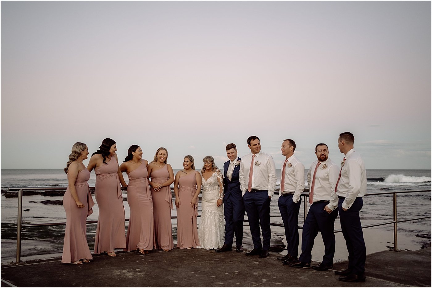 Bridal party standing at Merewether Baths at sunset together