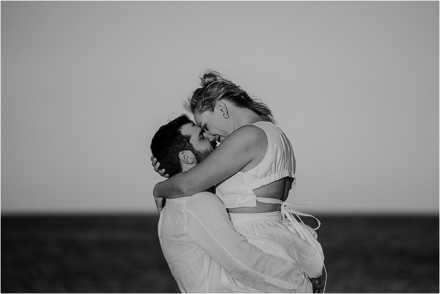 A black and white photo of a couple hugging on the beach.