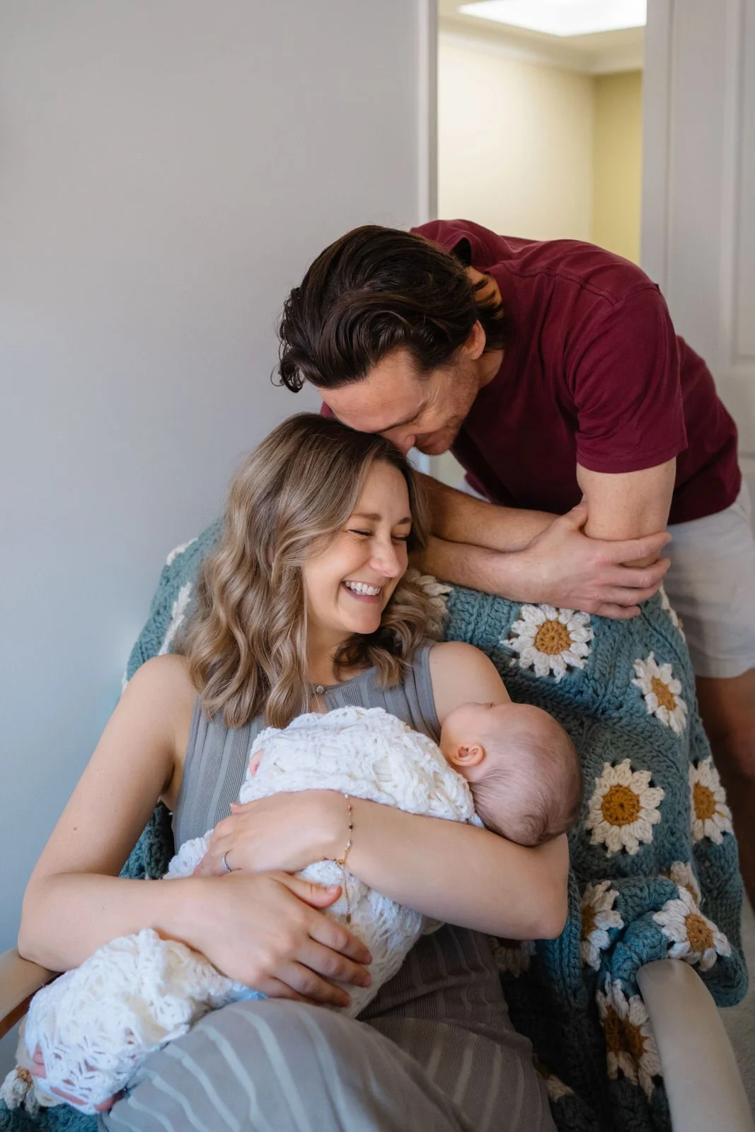 A woman holding a newborn baby and smiling as a man leans in to kiss her on the forehead.