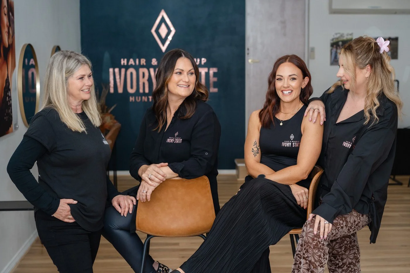 Group of four women standing and sitting together, wearing all black in a hair salon in Cessnock NSW
