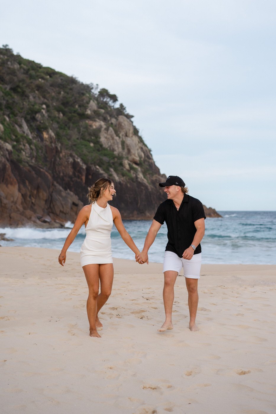 Couple walking along the beach, holding hands and looking at each other