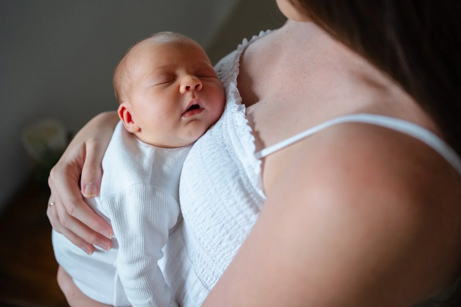 Close-up of a newborn baby sleeping on a woman's shoulder, with her hand supporting the baby and part of her shoulder and arm visible.