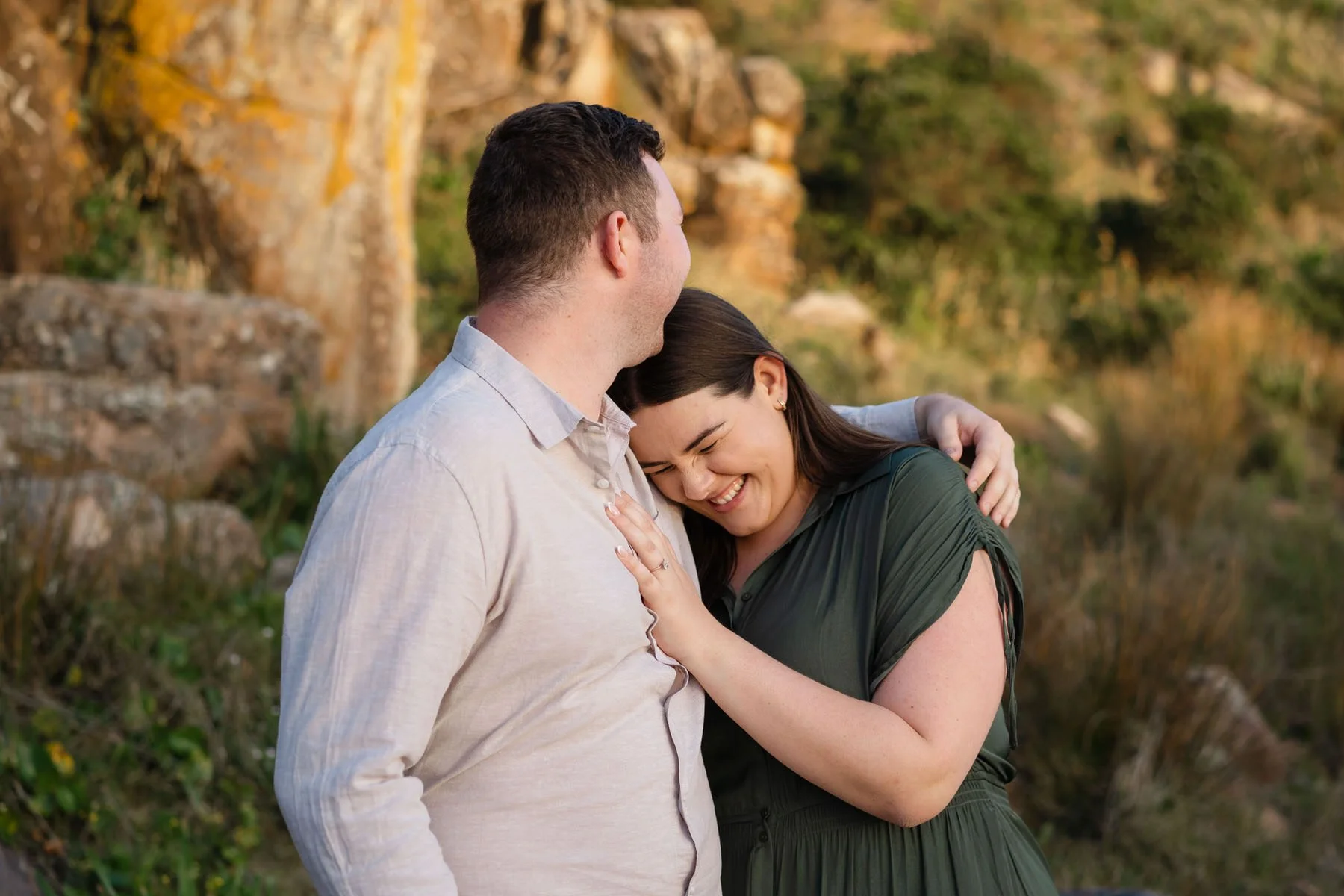 A couple sharing a happy moment outdoors, with the woman smiling and leaning into the man's chest.