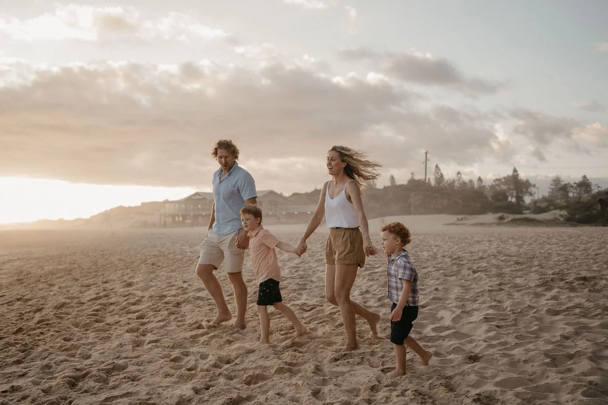 Family of four walking along the beach, holding hands at sunset