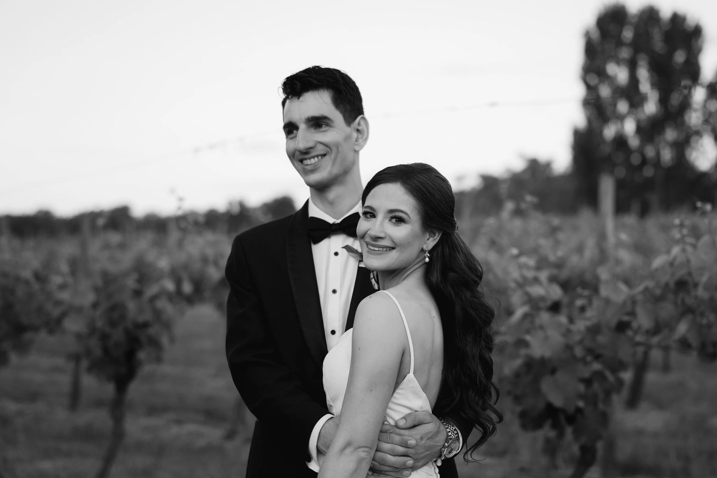 Black and white photo of a married couple standing in the vines at a Canberra vineyard