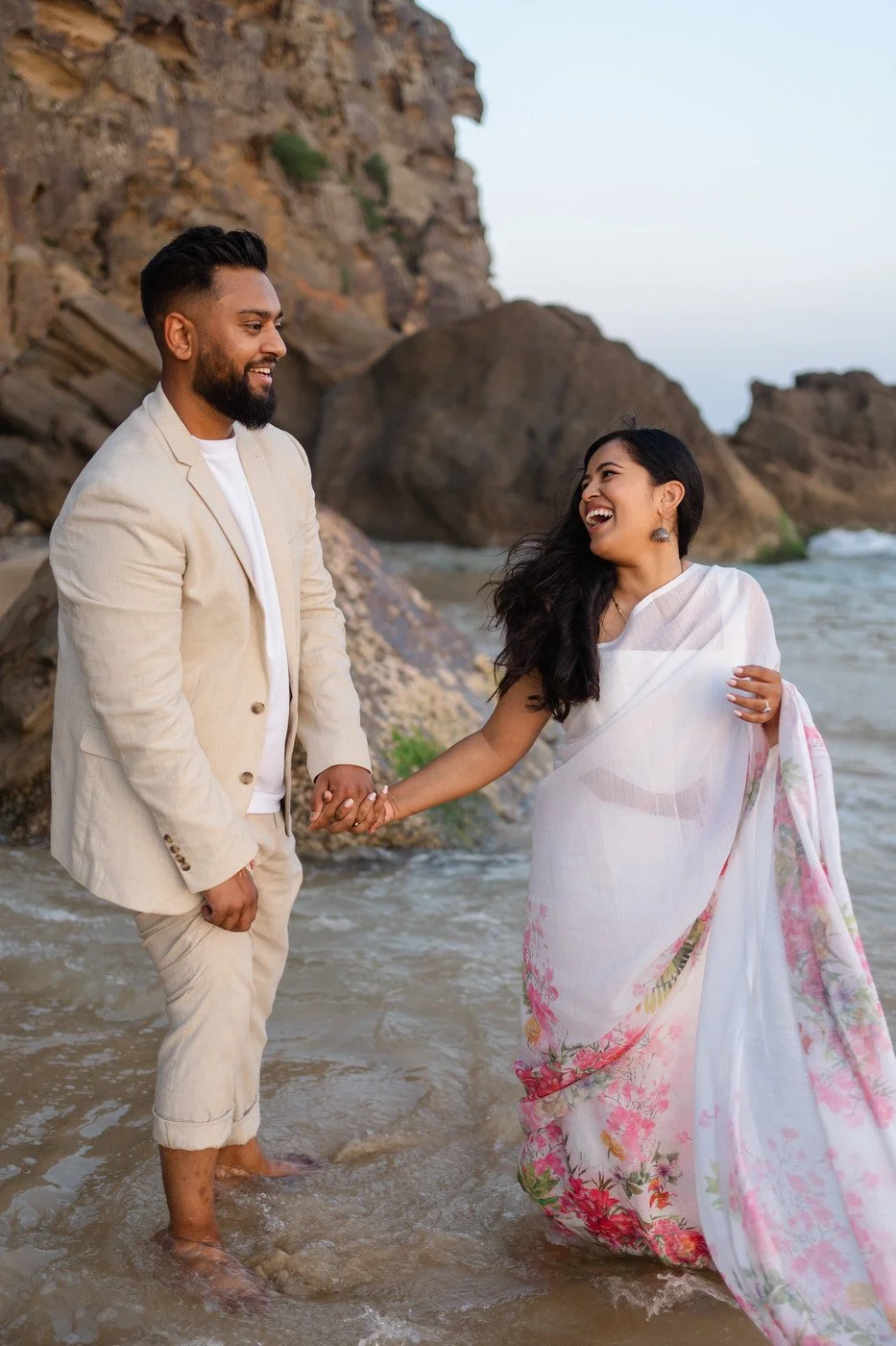 Indian couple walking along the water at Redhead beach, holding hands and laughing together