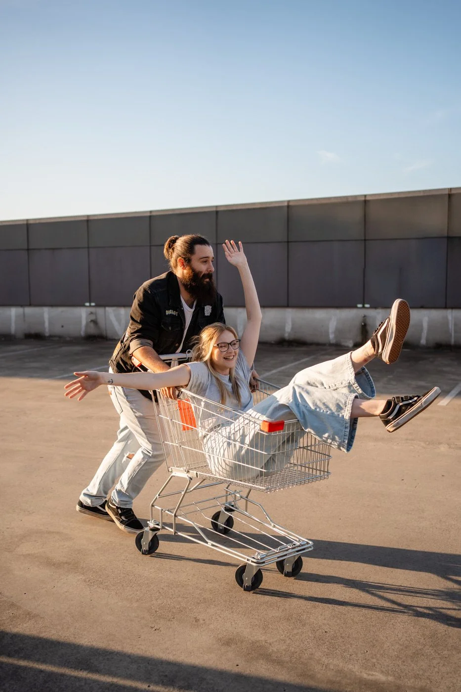 Woman sitting in a trolley, being pushed around by her partner on a shopping rooftop. Both are laughing and smiling