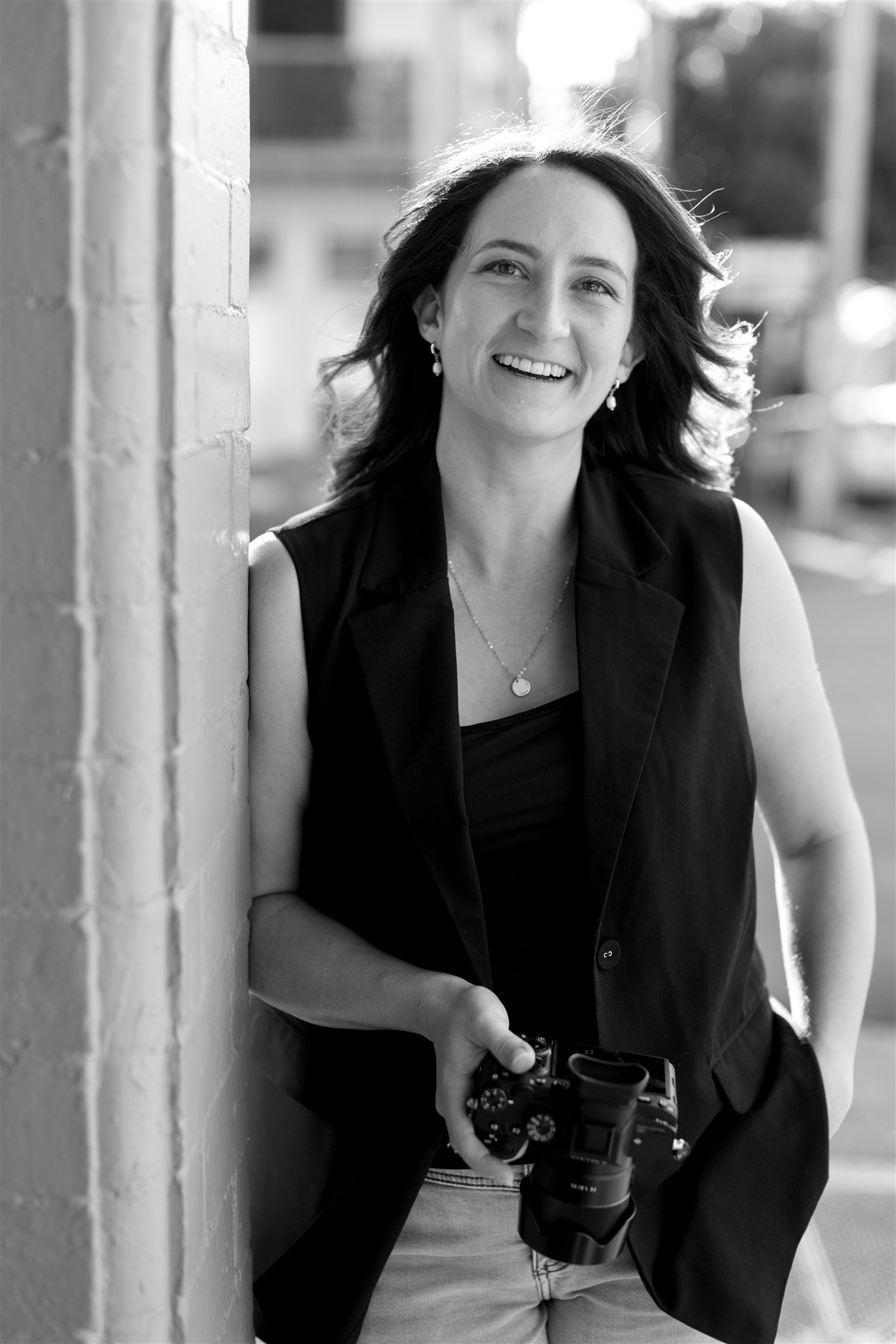 newcastle wedding photographer standing against a wall holding a camera and smiling