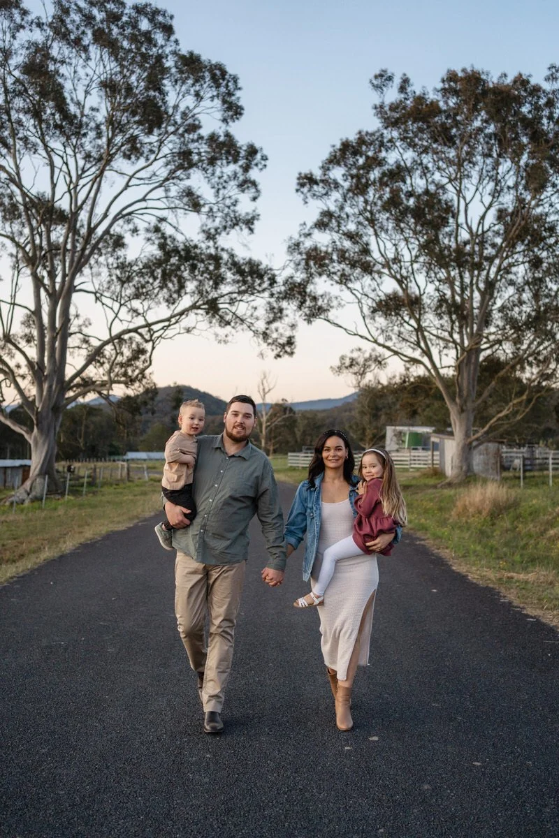 family with two young children, holding hands and walking down a black tar road together