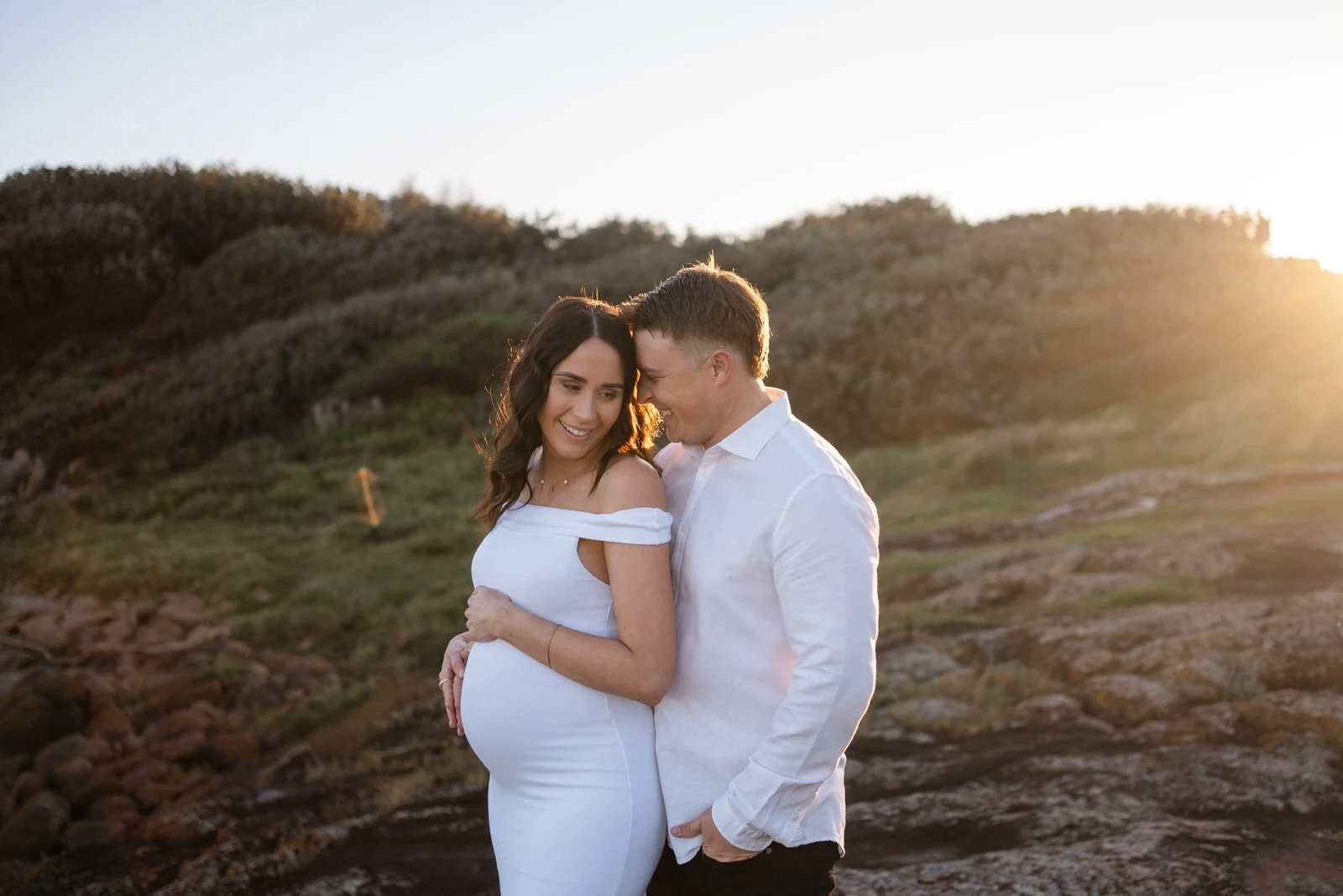pregnant woman and partner hugging whilst standing on the rocks at Birubi beach, Port Stephens