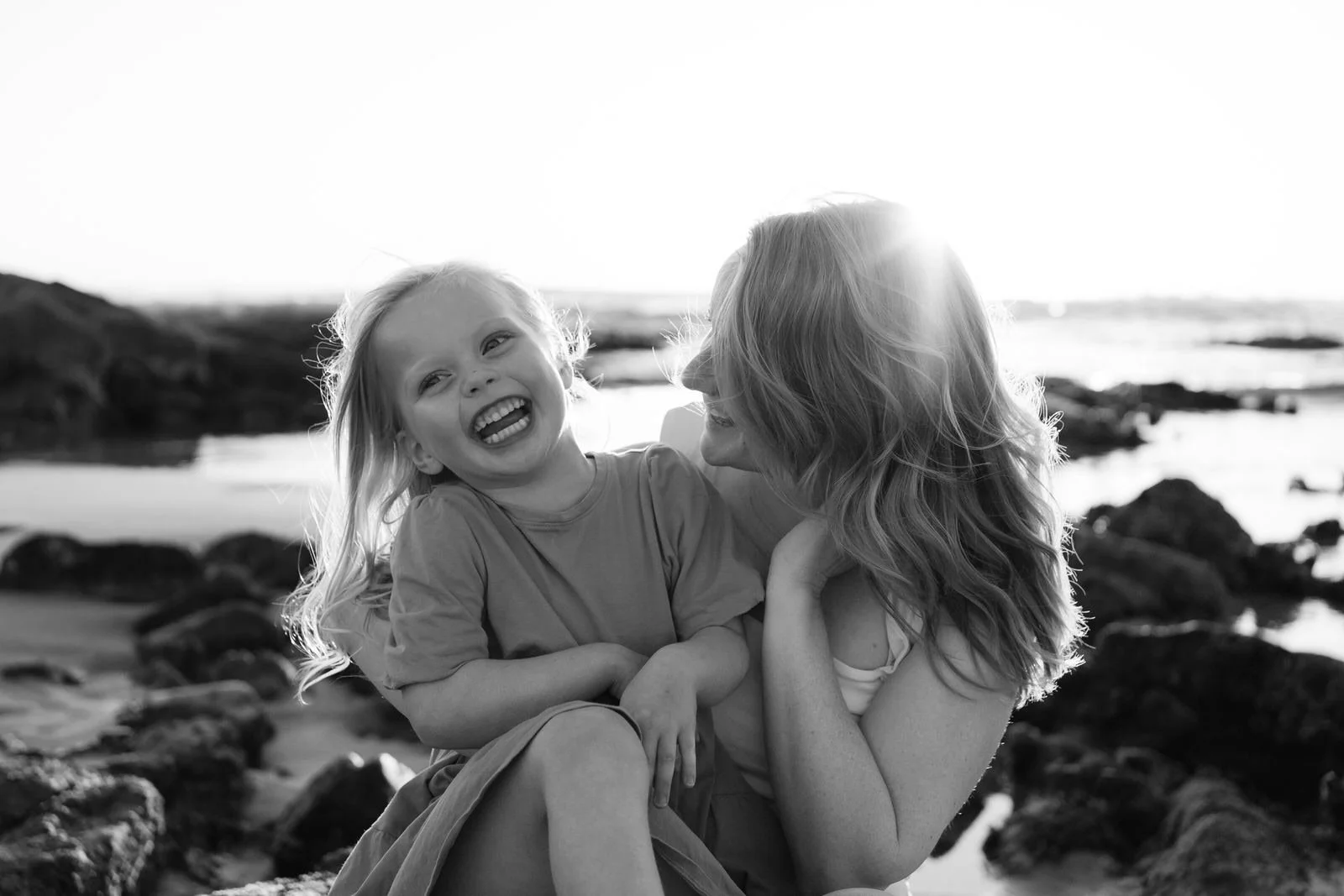 Mother and daughter laughing together, sitting on the rocks at Birubi beach, Port Stephens