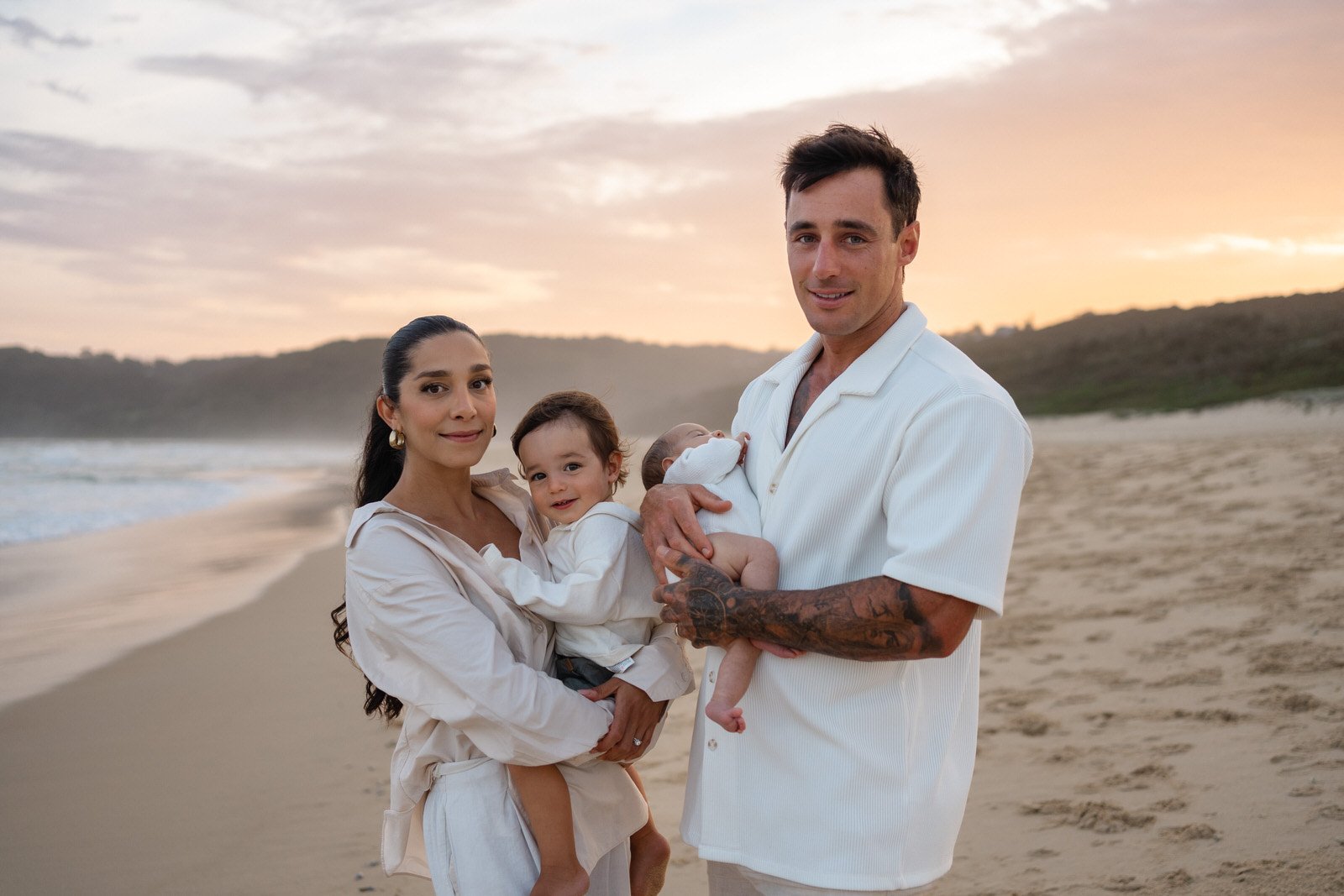 Family with two young children, standing on the beach together at sunset