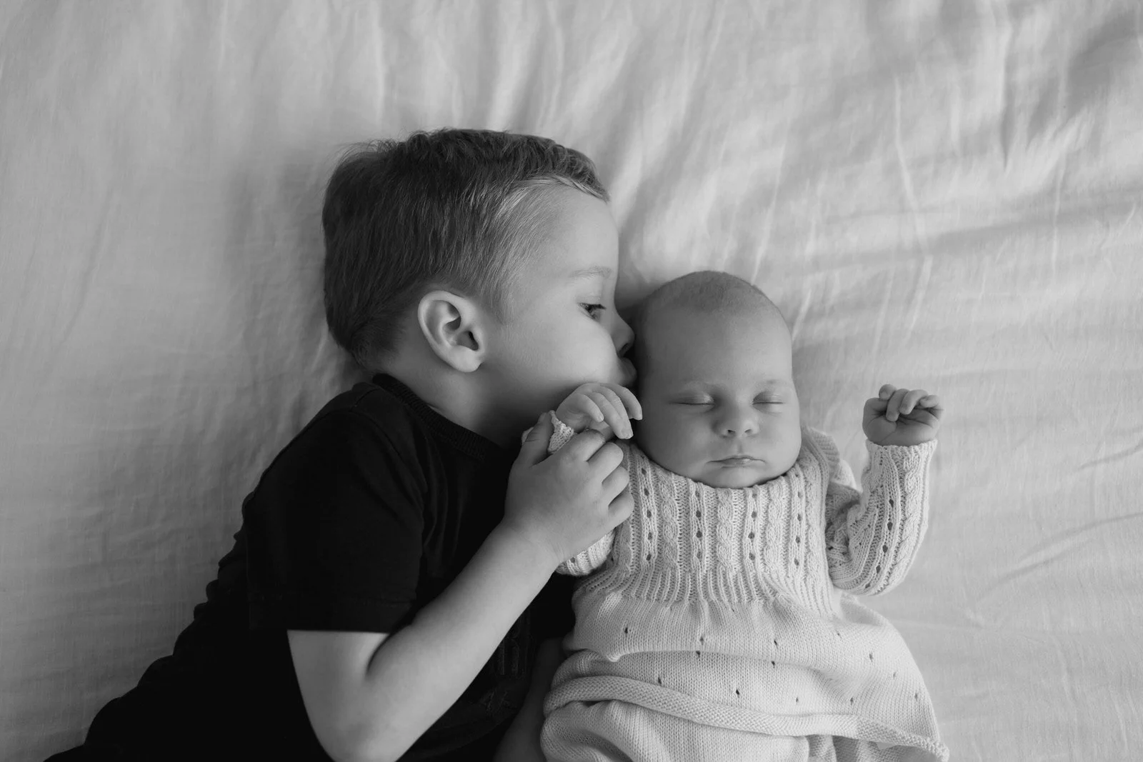 A young boy is kissing a sleeping baby on the forehead while lying on a bed.