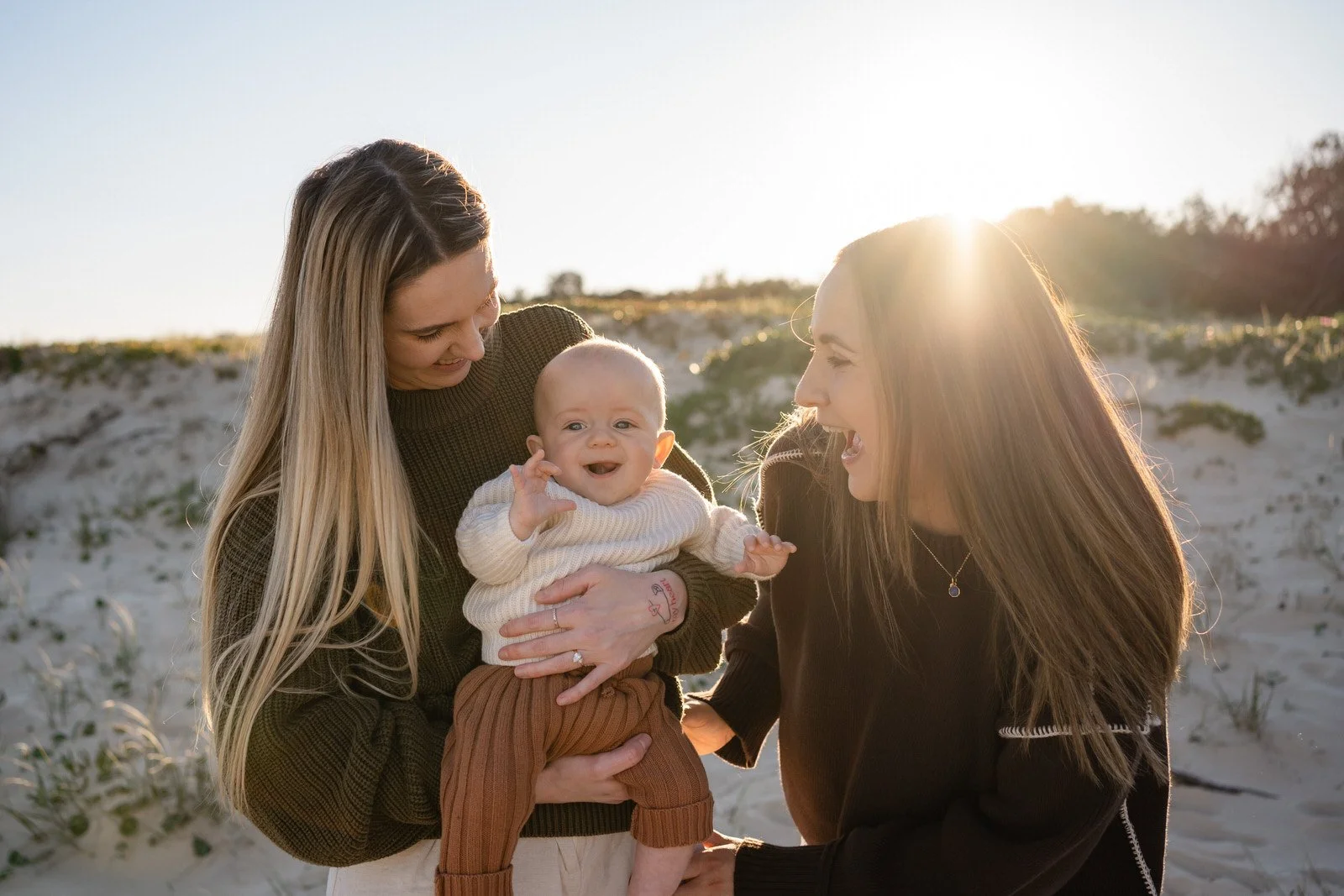 Couple and baby standing on the sand at the beach, hugging and smiling at their baby