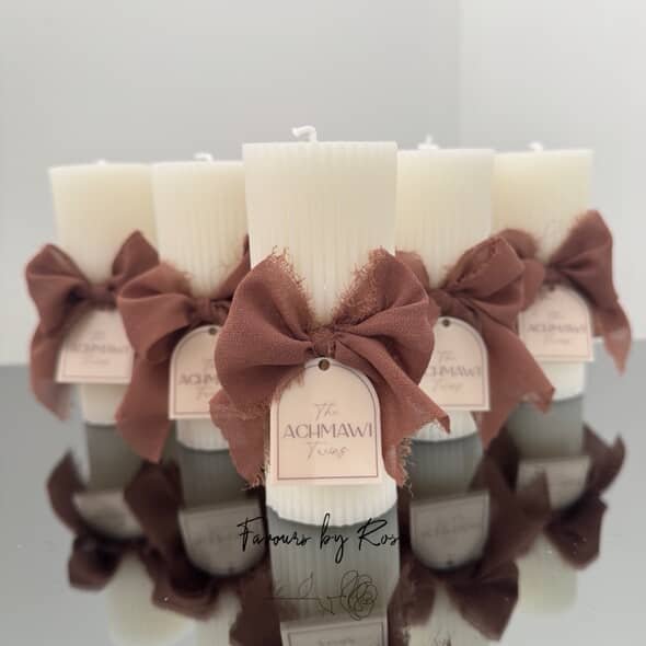 Four white candles wrapped with brown fabric and tied with brown bows, positioned on a reflective surface.