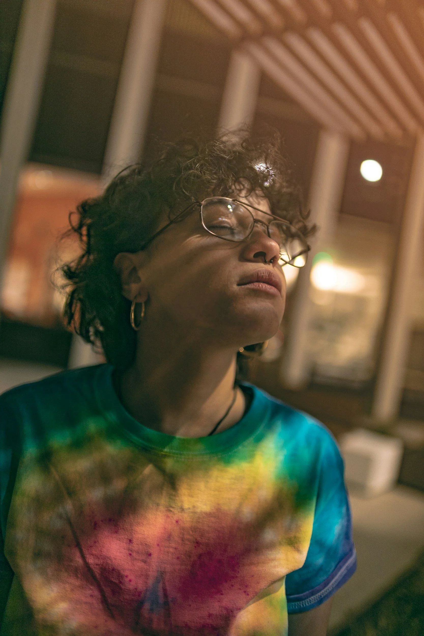 A BIPOC Queer adult looking upward surrounded by light representing growth and healing