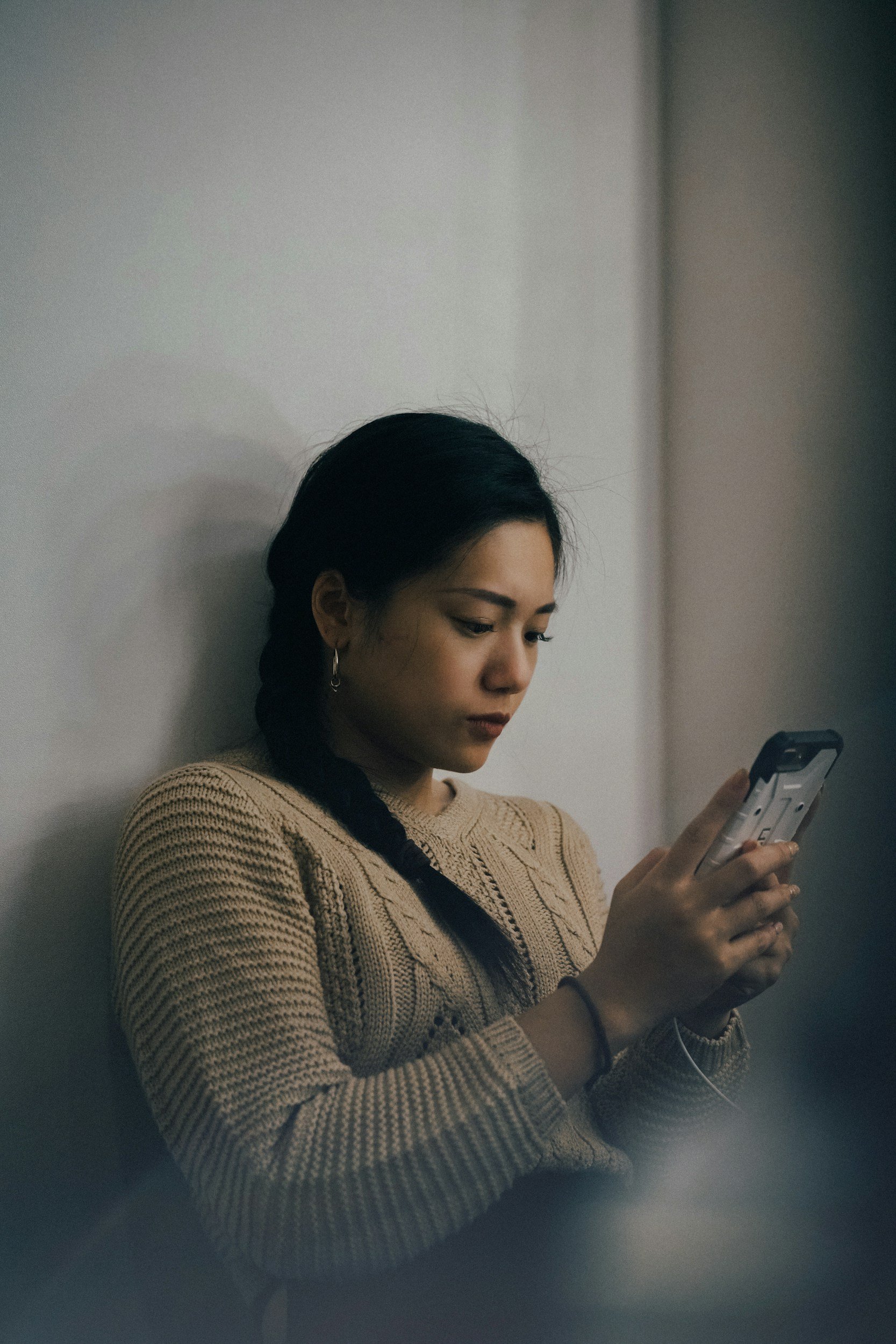 Person wearing a sweater looking at phone hesitating before responding to a text message