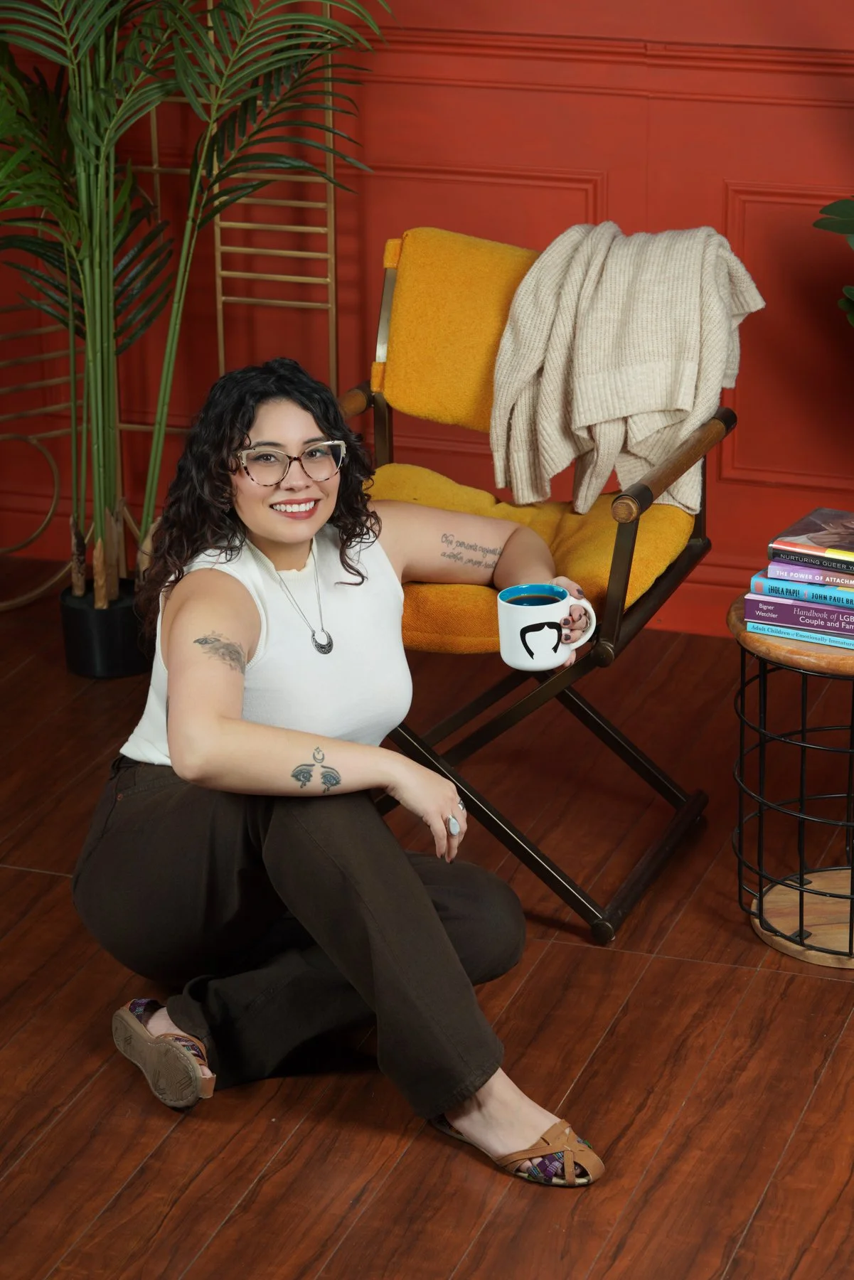 image of relationship therapist in los angeles for anxiety wearing glasses with tattoos around plants in front of yellow chair