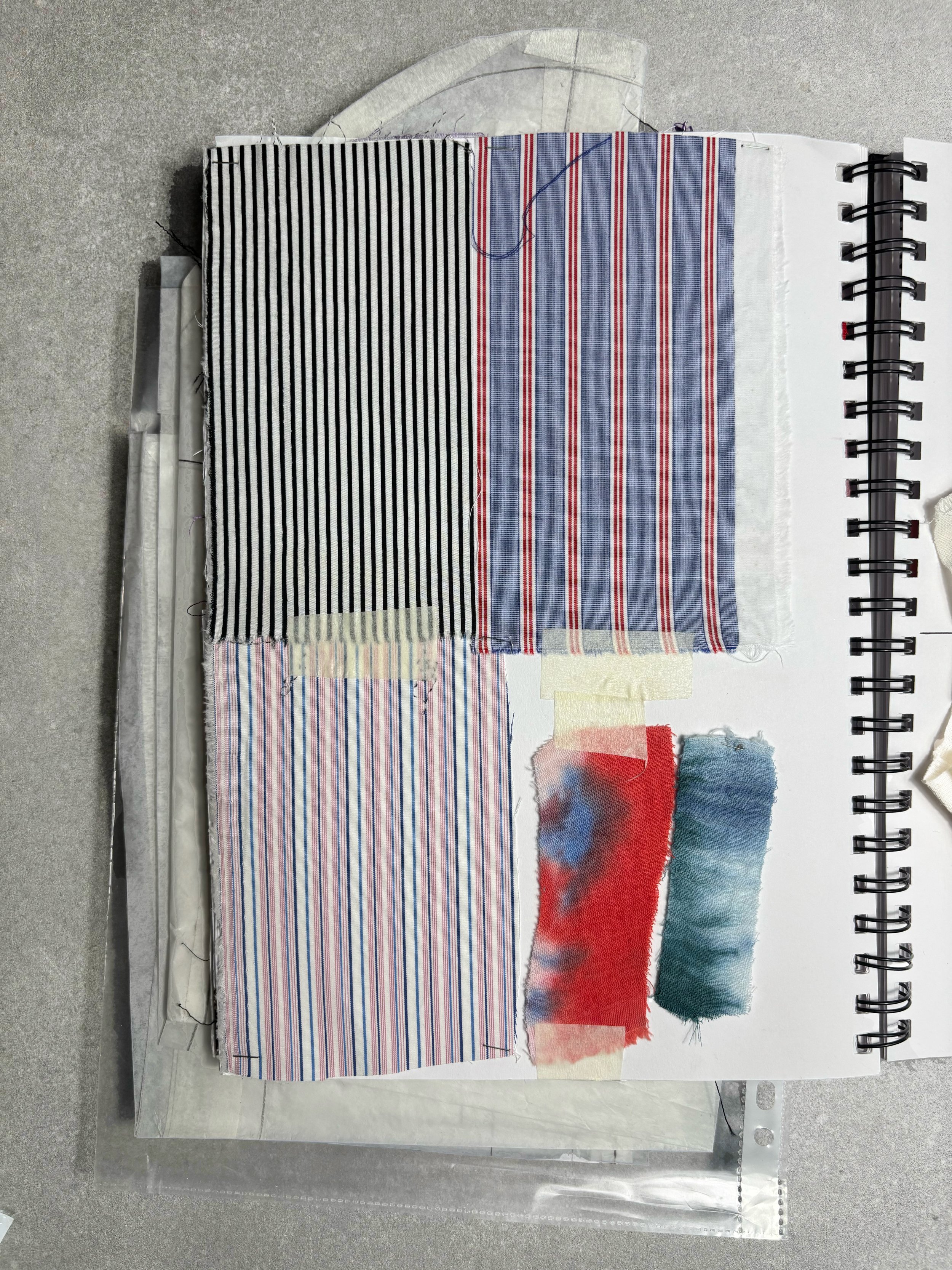 Échantillons de tissus à rayures en couleurs variées, disposés sur un carnet de croquis. Certains tissus sont enroulés ou fixés avec du ruban adhésif.