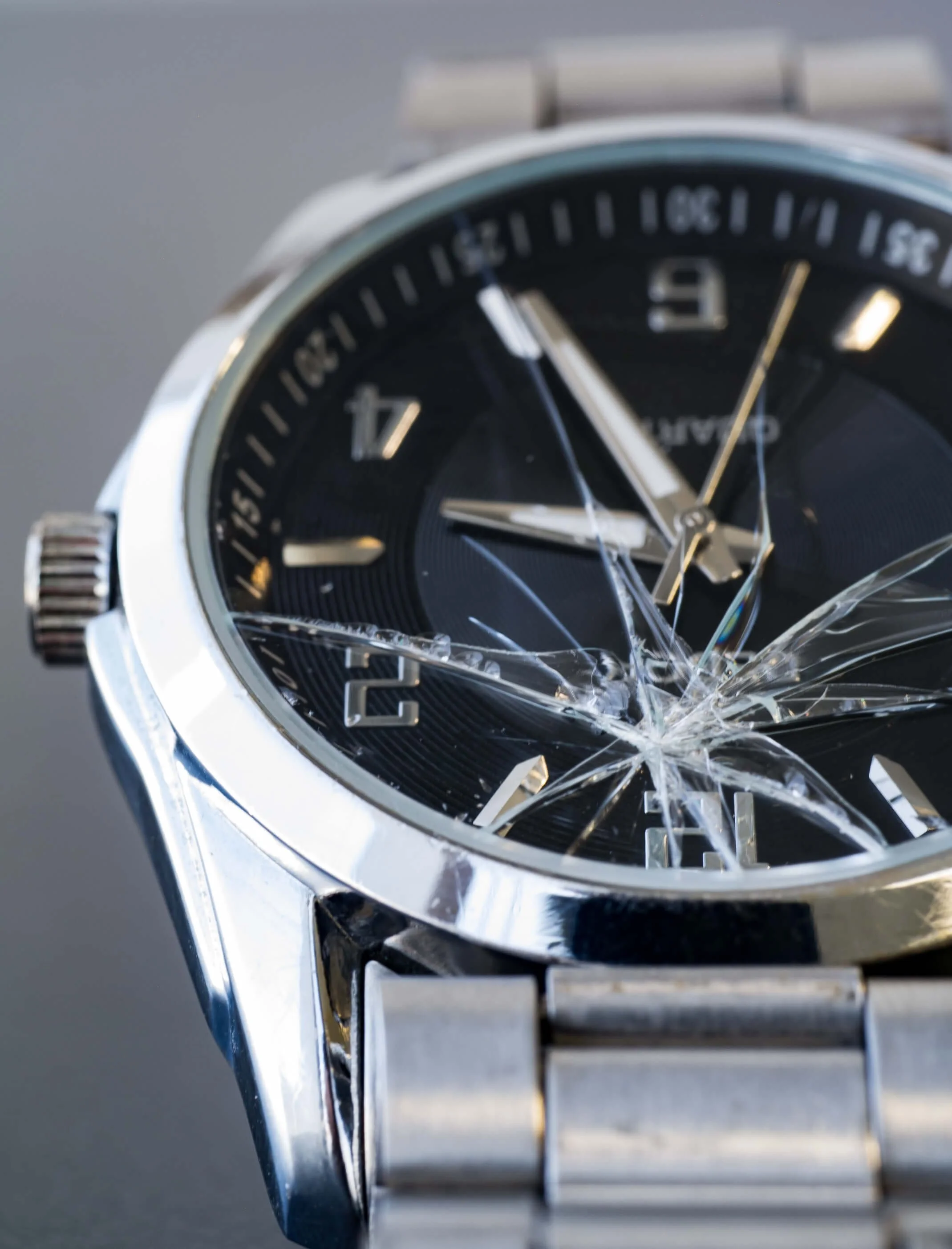 Close-up of a broken wristwatch with a shattered glass face, showing the time as approximately 10:09.
